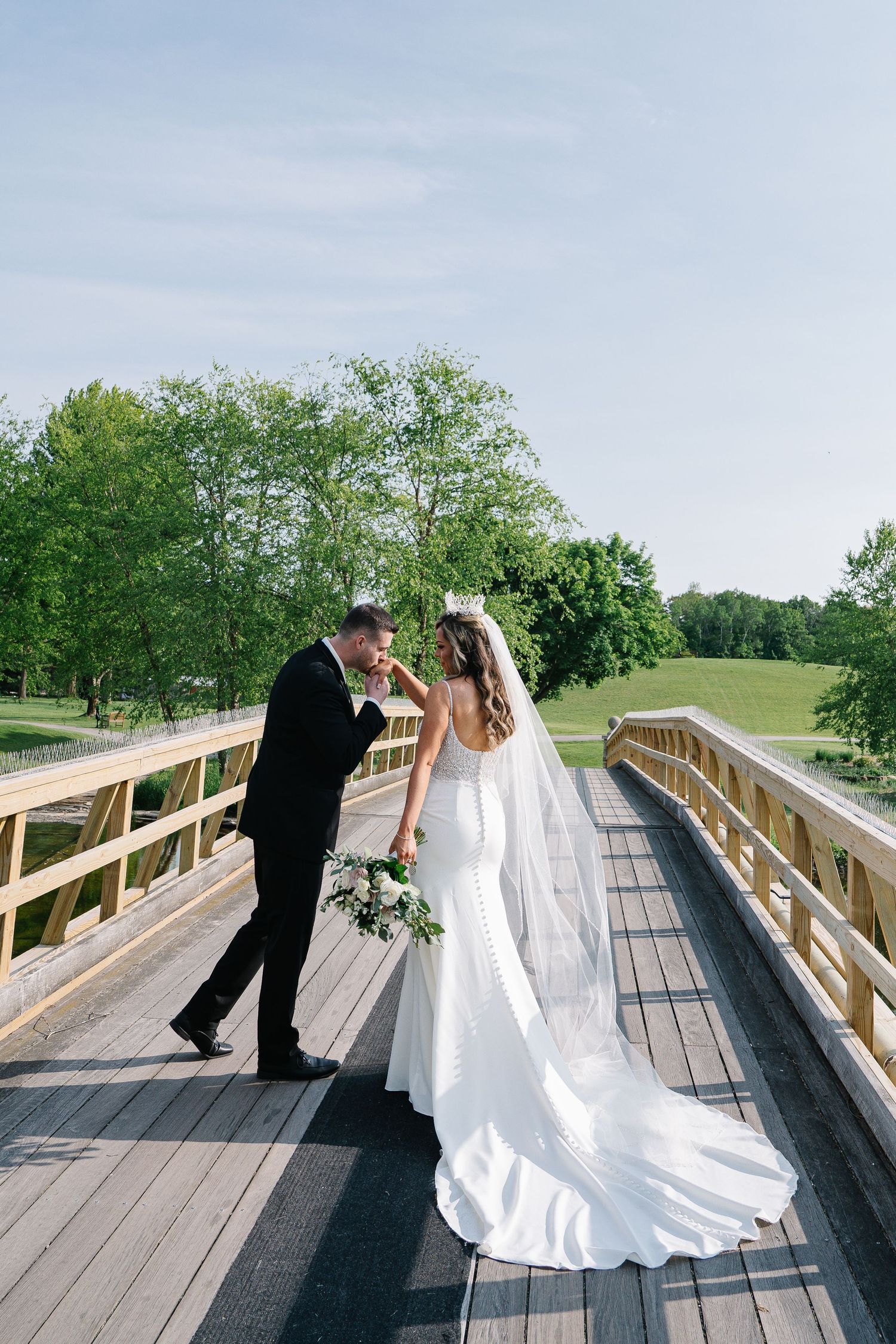 Wedding couple shares a romantic moment on a wooden bridge surrounded by greenery.