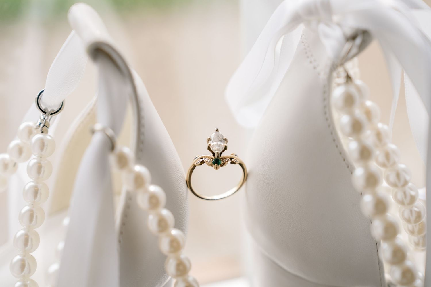 Delicate diamond engagement ring balanced between pearl necklace strands against white fabric background.