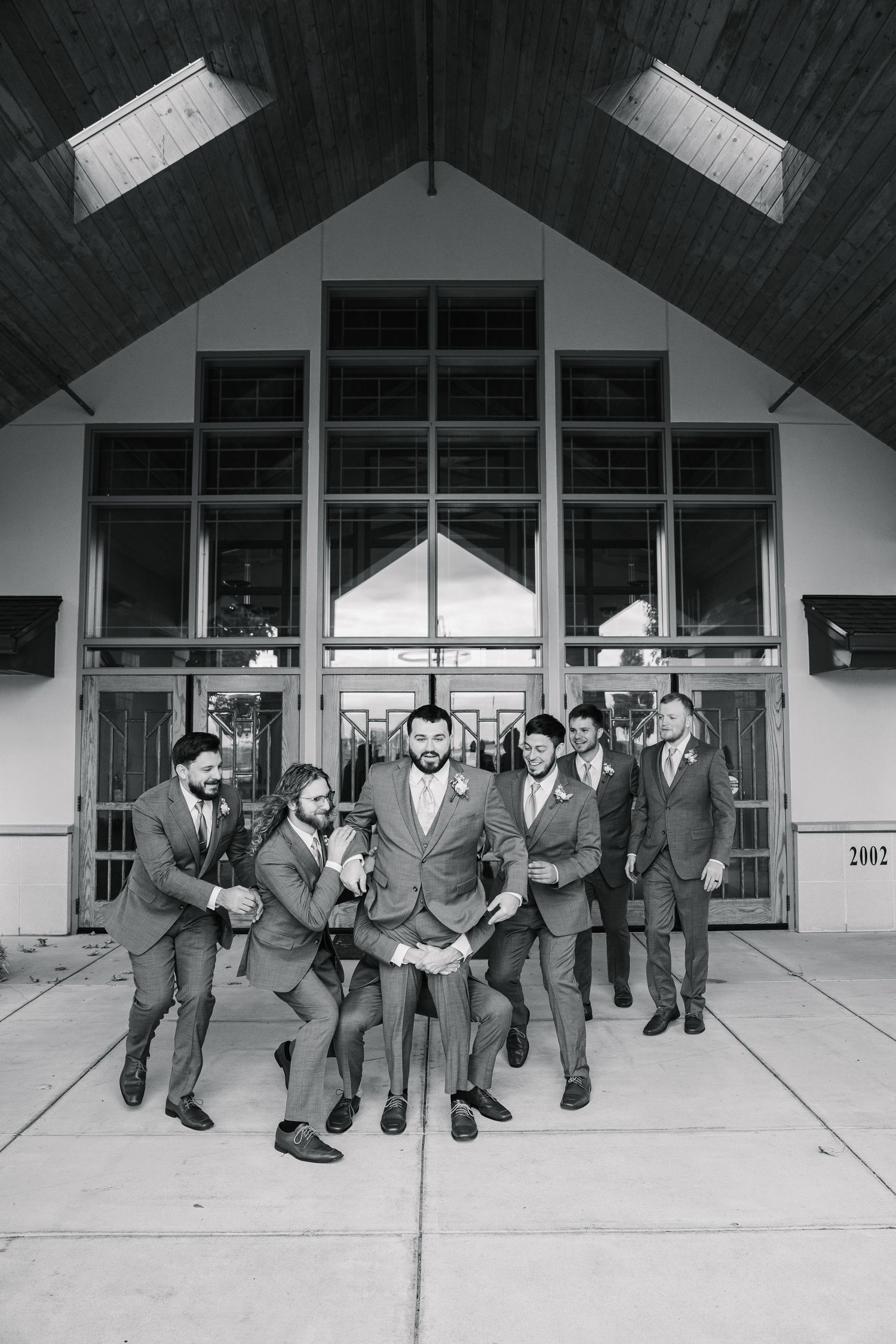 A sequence of black and white photos showing groomsmen performing a synchronized jumping dance move outside a building.