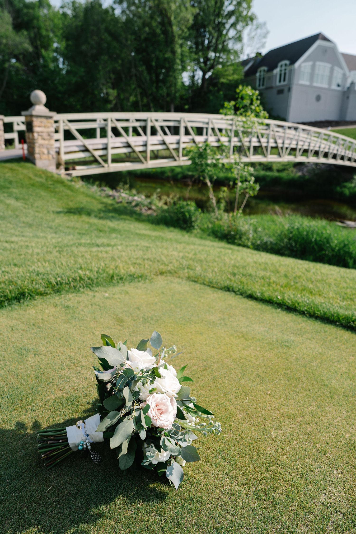 White floral bouquet lying on grass with a wooden bridge and house in the background.