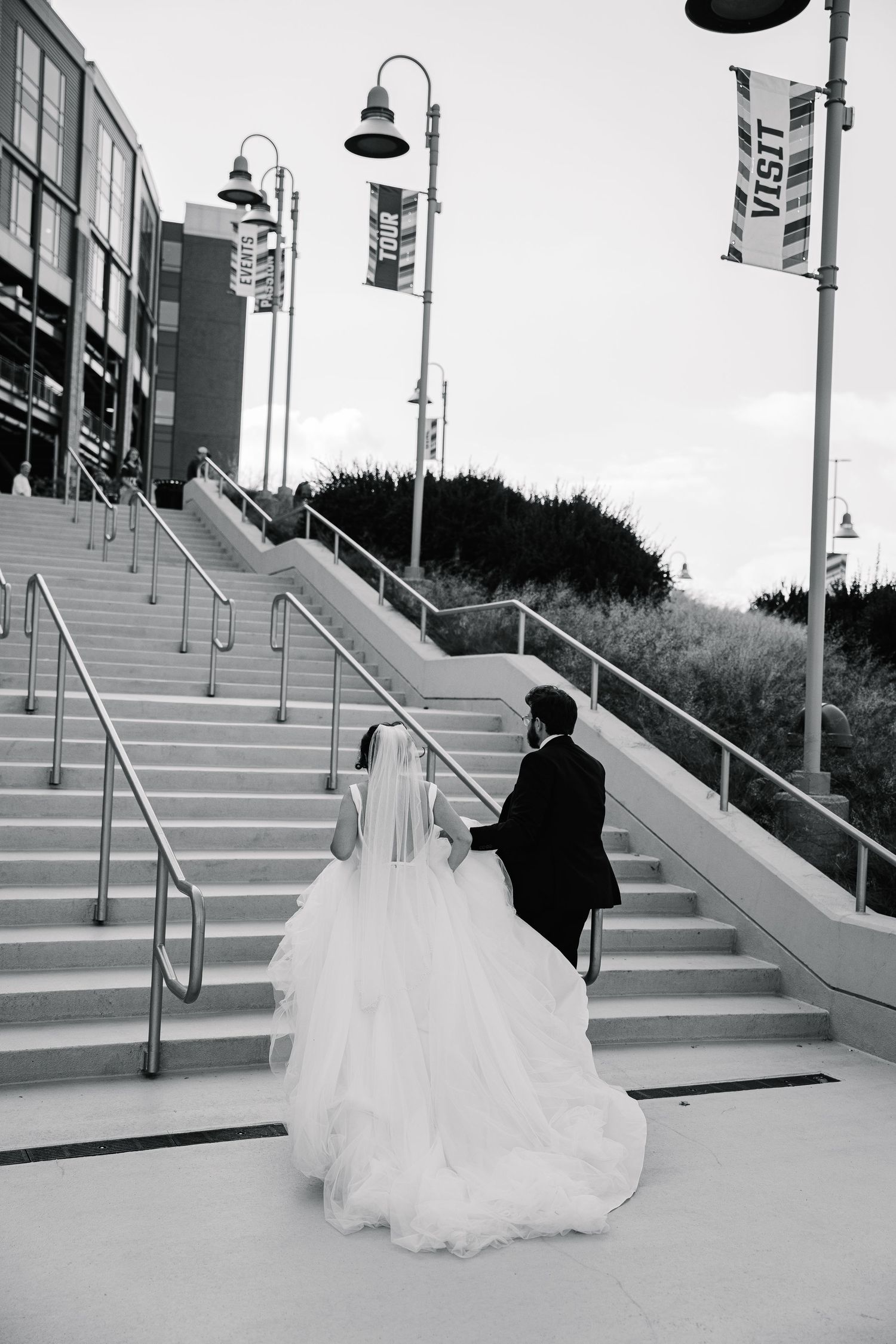 Black and white photo of couple ascending outdoor stairs with decorative lampposts.