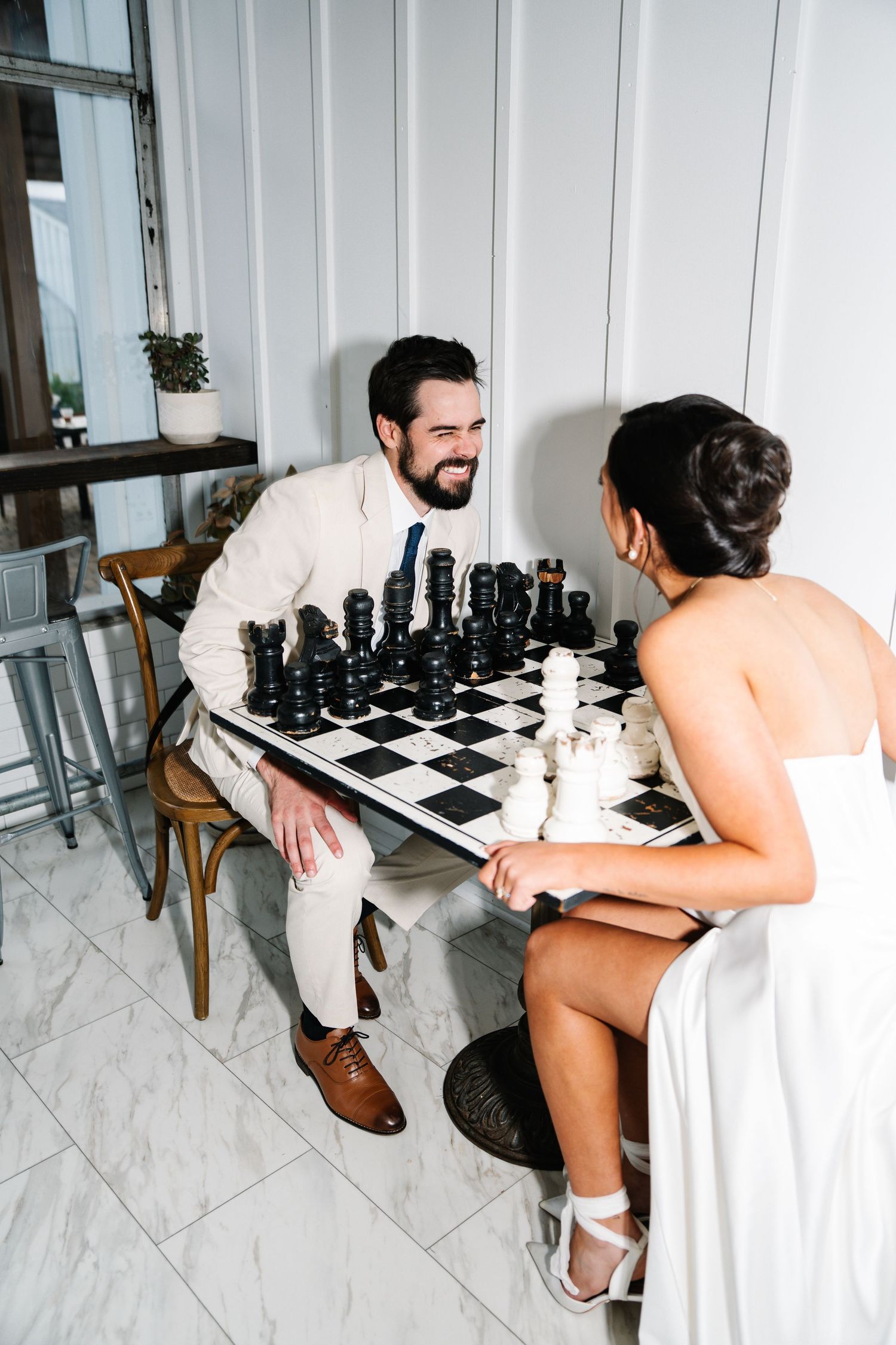 Two people playing chess on a white marble floor with black chess pieces arranged on a checkered board.