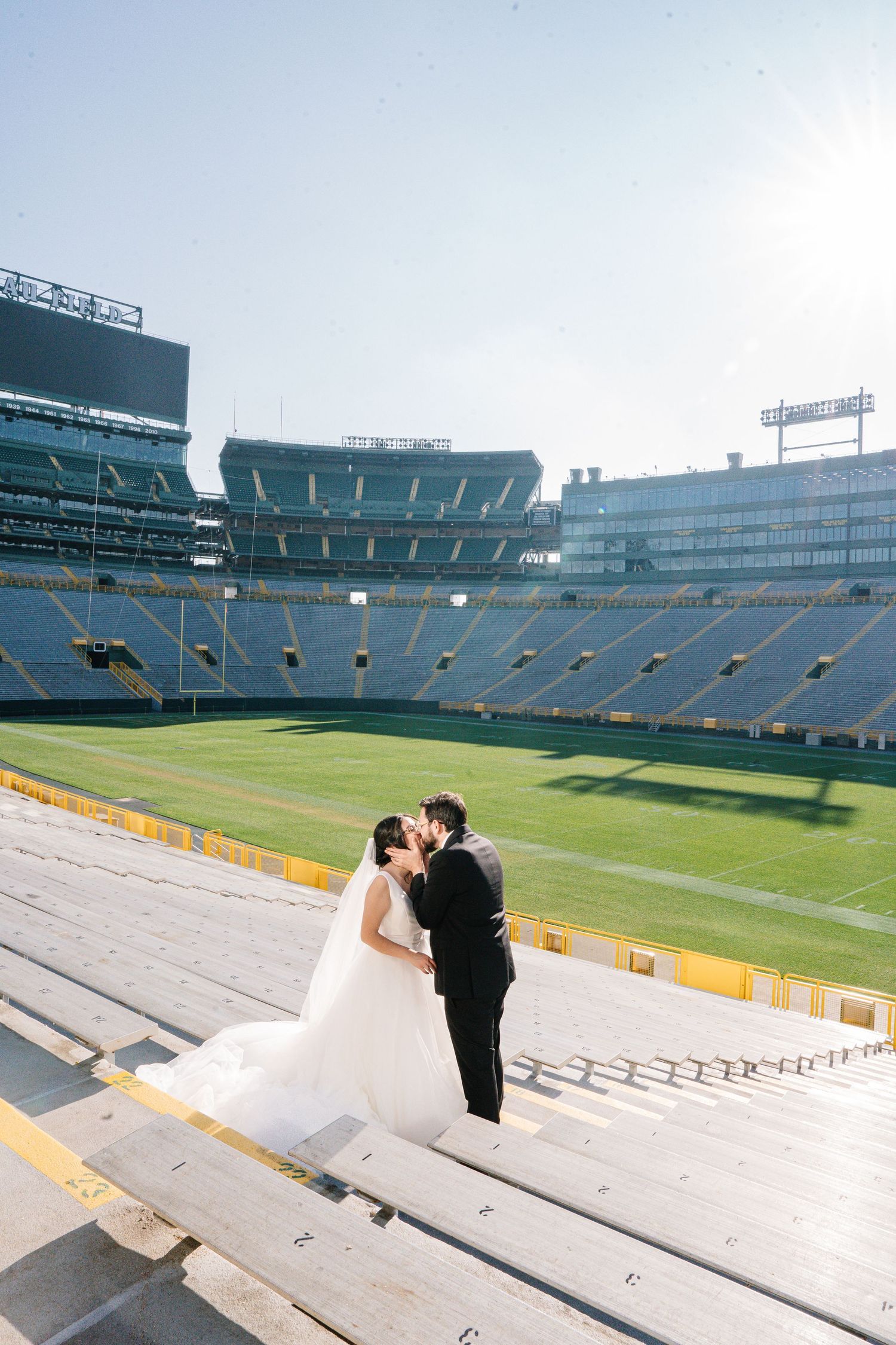 A couple poses for photos on the concrete bleachers of an empty professional football stadium.