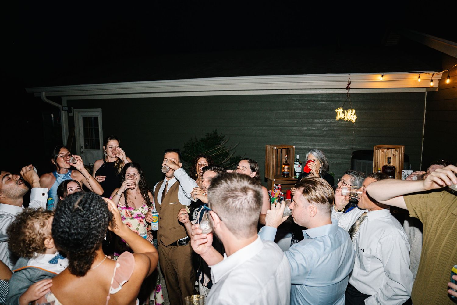 A lively crowd of wedding guests dancing and celebrating together on a dark dance floor at an evening reception.