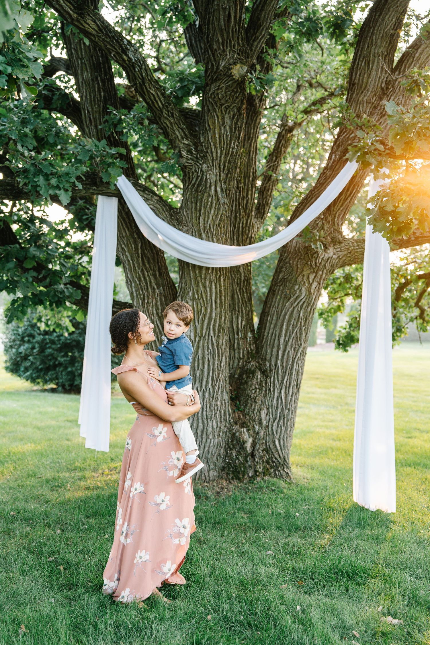 White fabric drapes elegantly between trees in a sunlit garden setting creating a romantic outdoor scene.