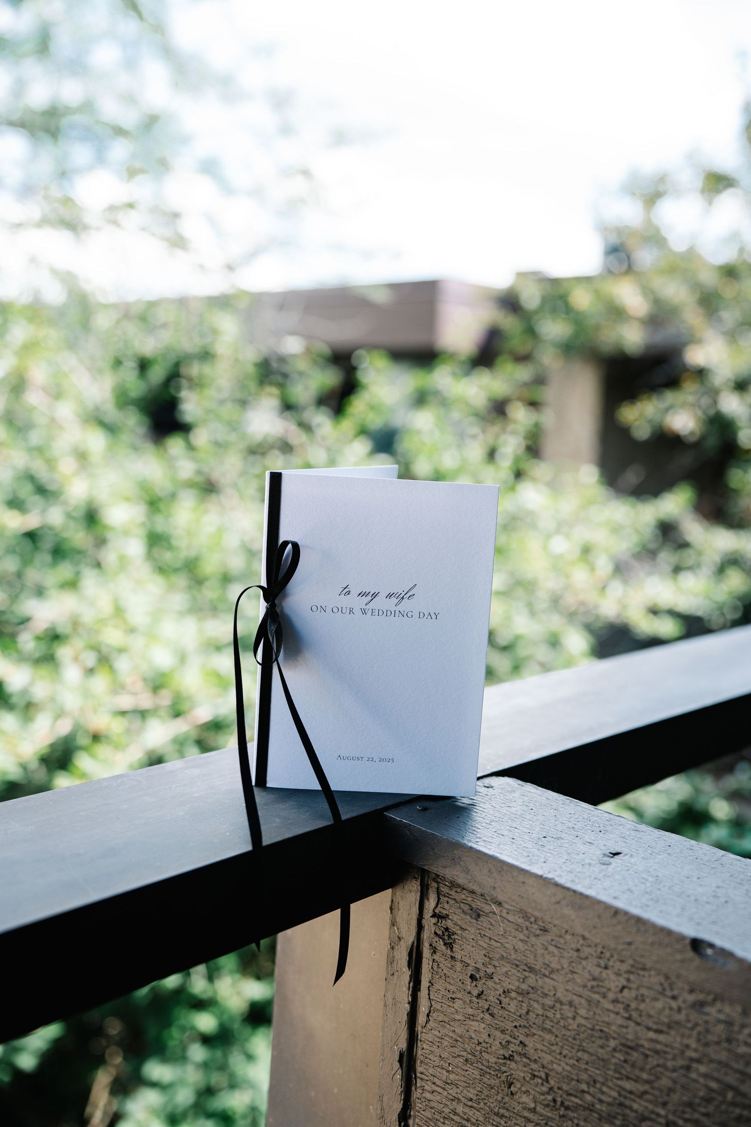 Three minimalist photos show a simple white card with black ribbon against a blurred green background outdoors.