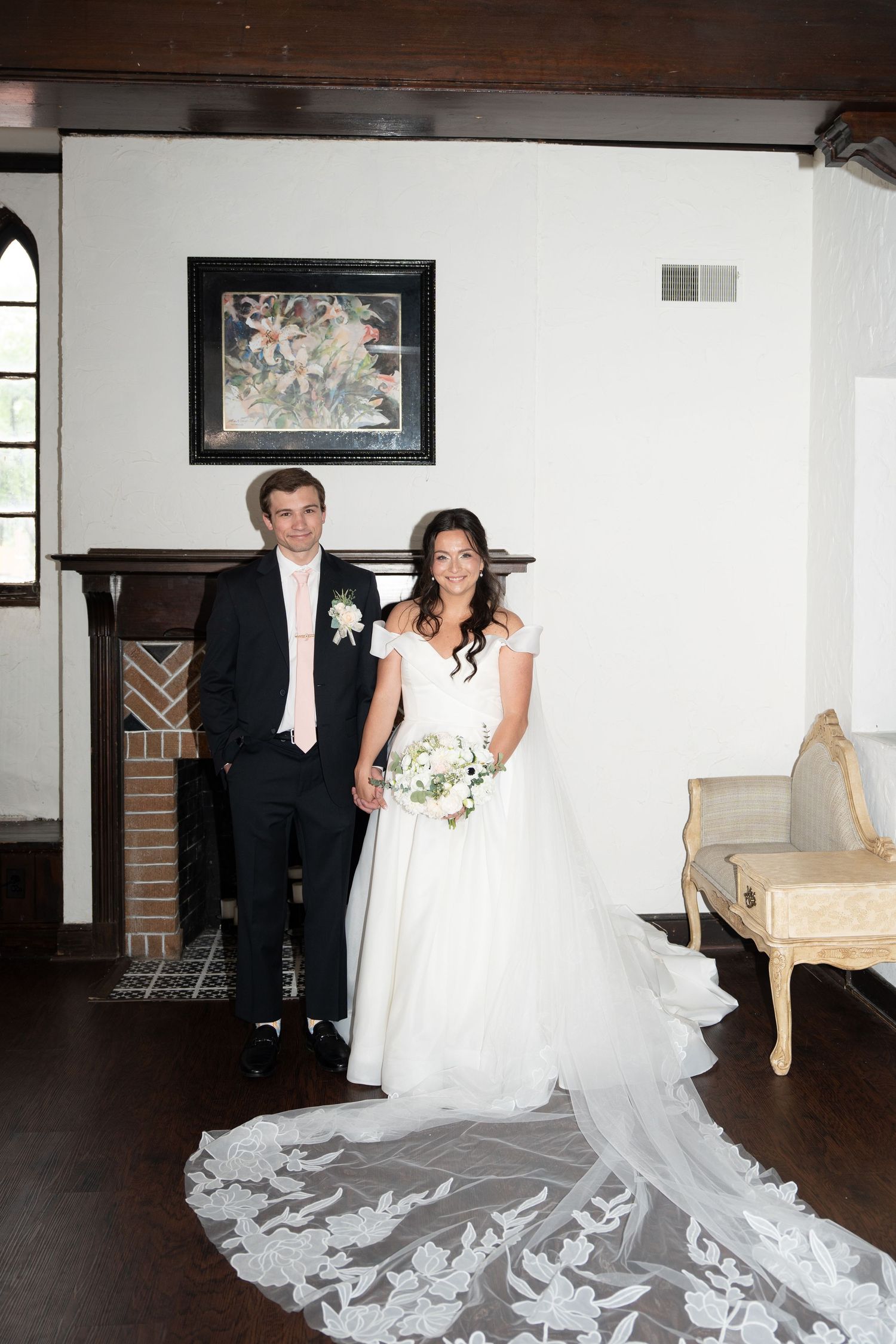A wedding scene showing a flowing white bridal gown with a dramatic long train on a dark hardwood floor.
