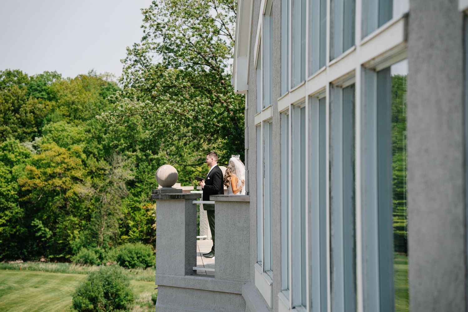 Modern architectural details of a white building with glass windows against a green landscape backdrop.