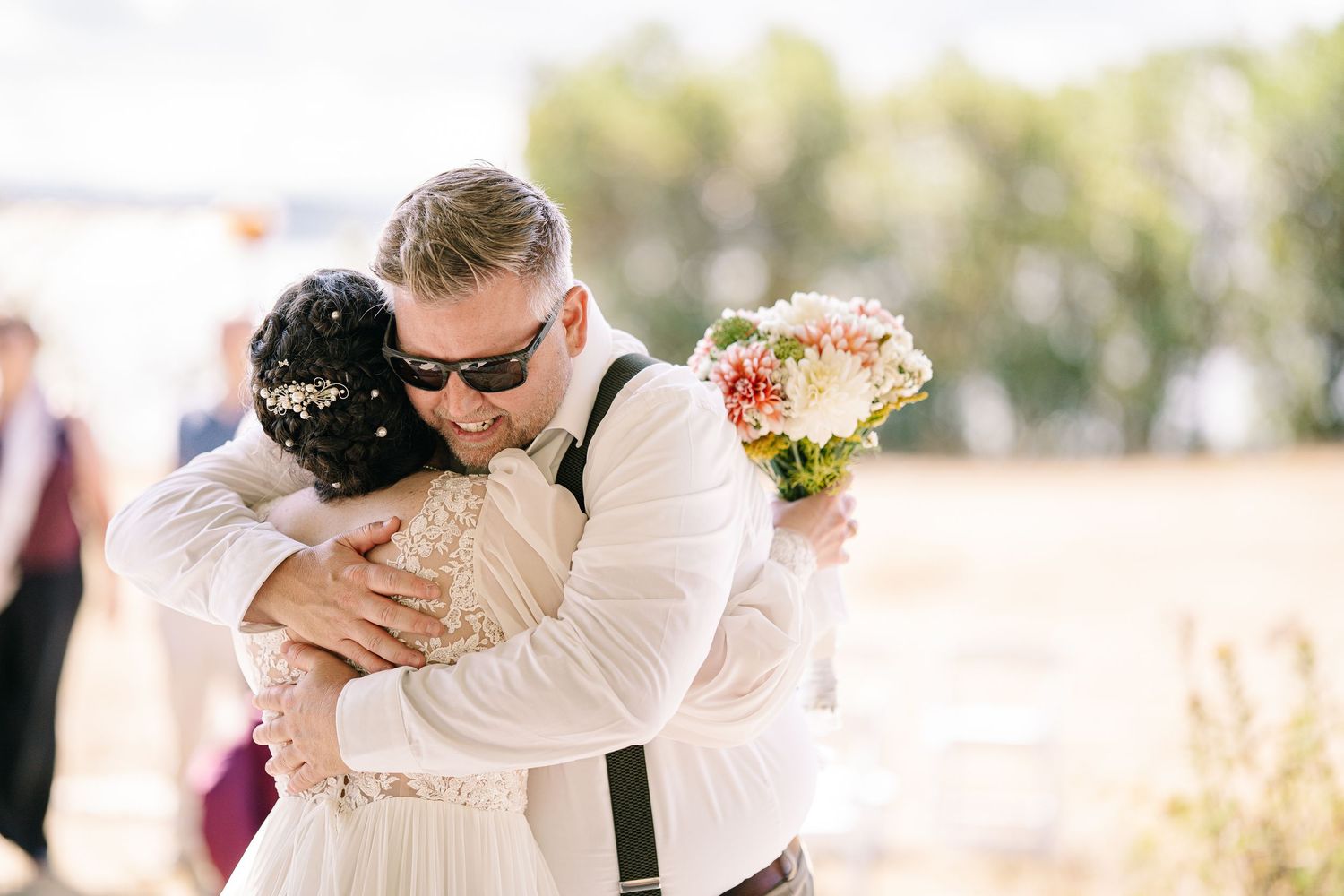 A romantic wedding couple embraces in a sun-drenched outdoor setting during their special day.