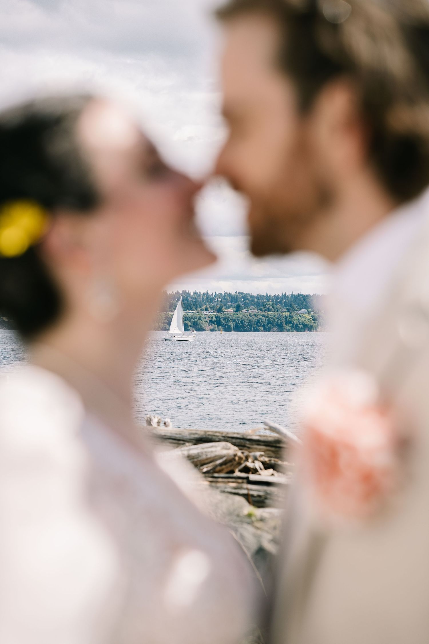 A romantic wedding moment captured by the water with sailboats and mountains in the background.