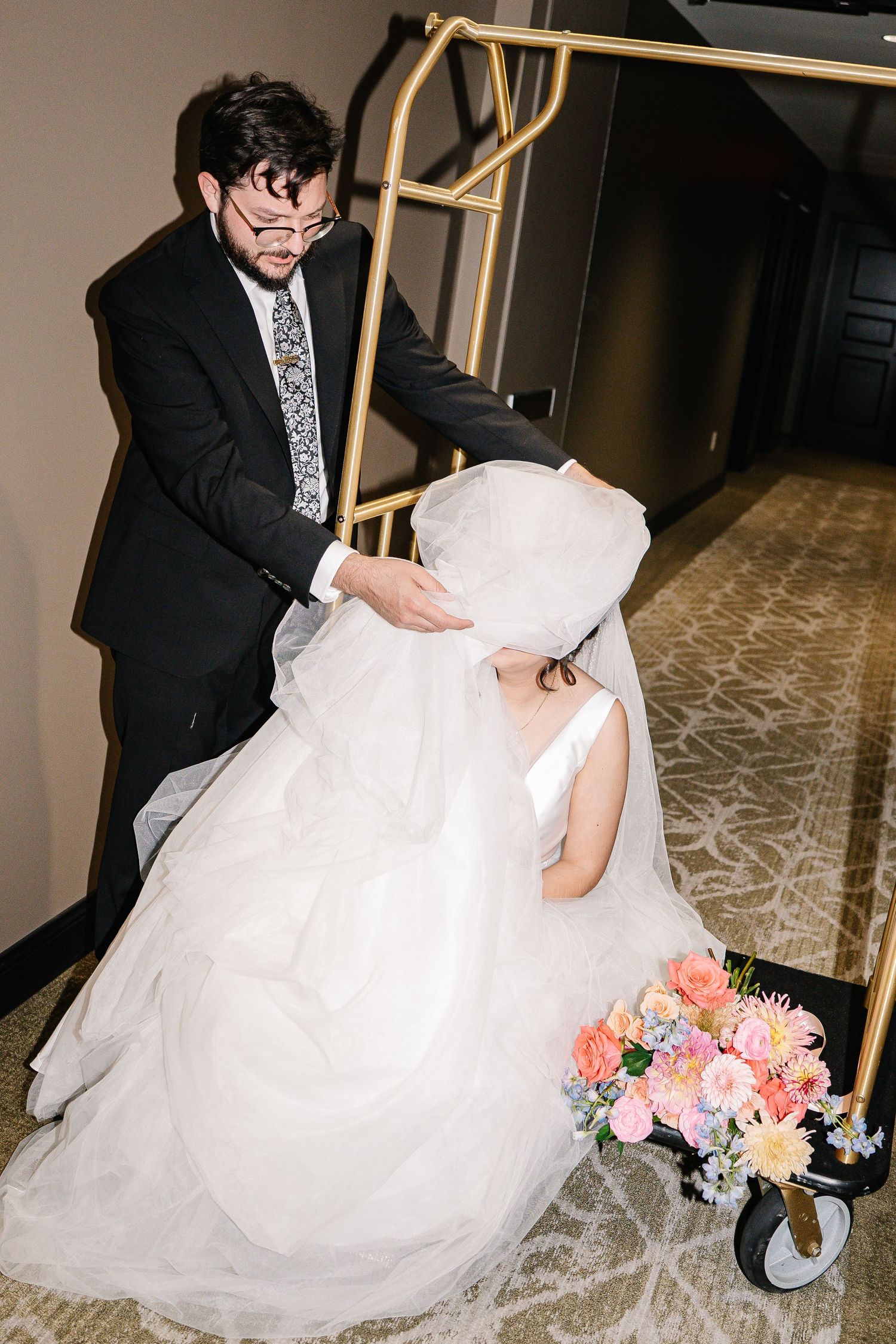 Wedding couple playfully interacting in a hotel hallway with the bride's flowing white gown and colorful bouquet.