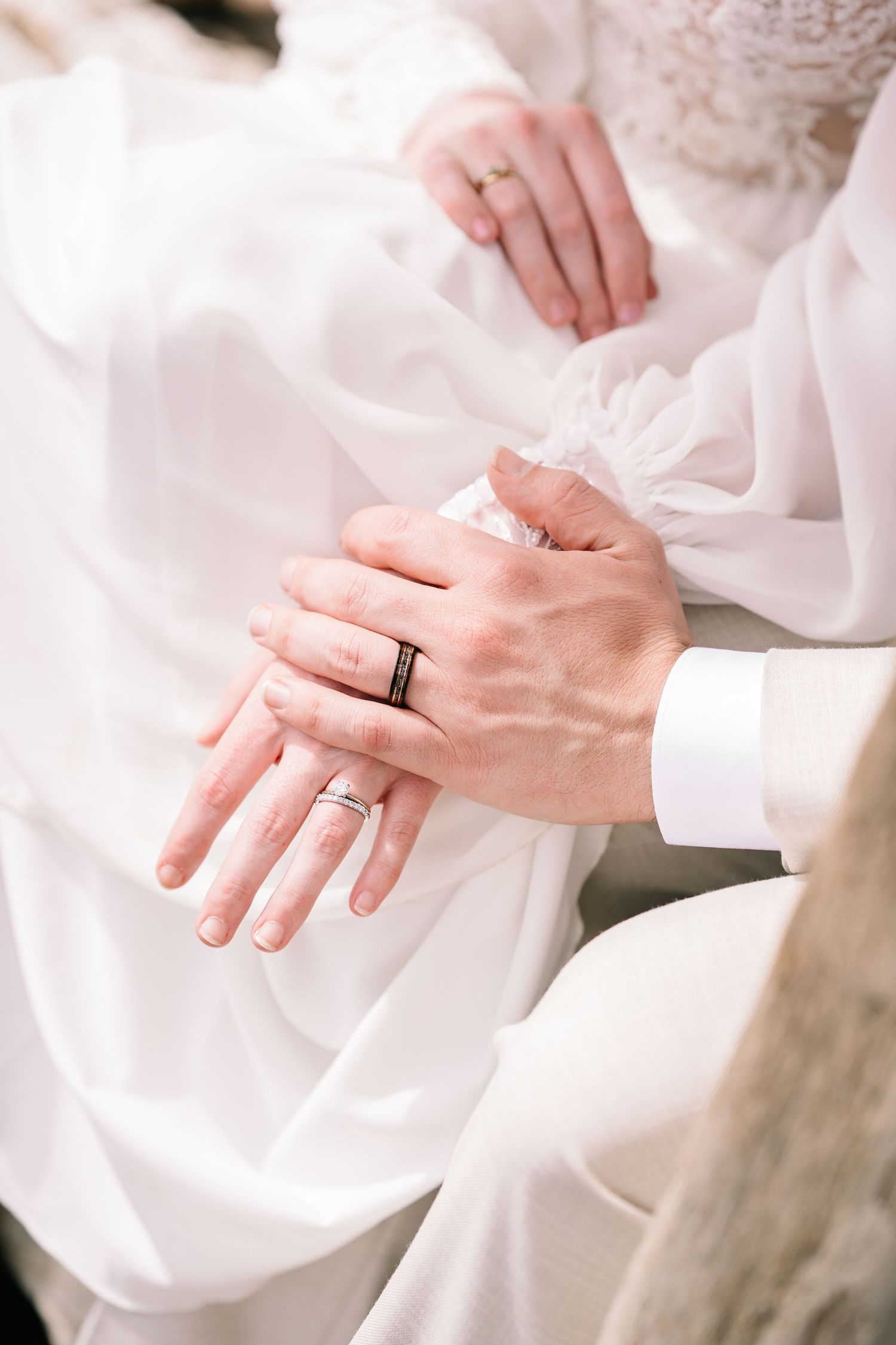 Close-up view of hands with wedding rings against white fabric showing delicate details and romantic styling.
