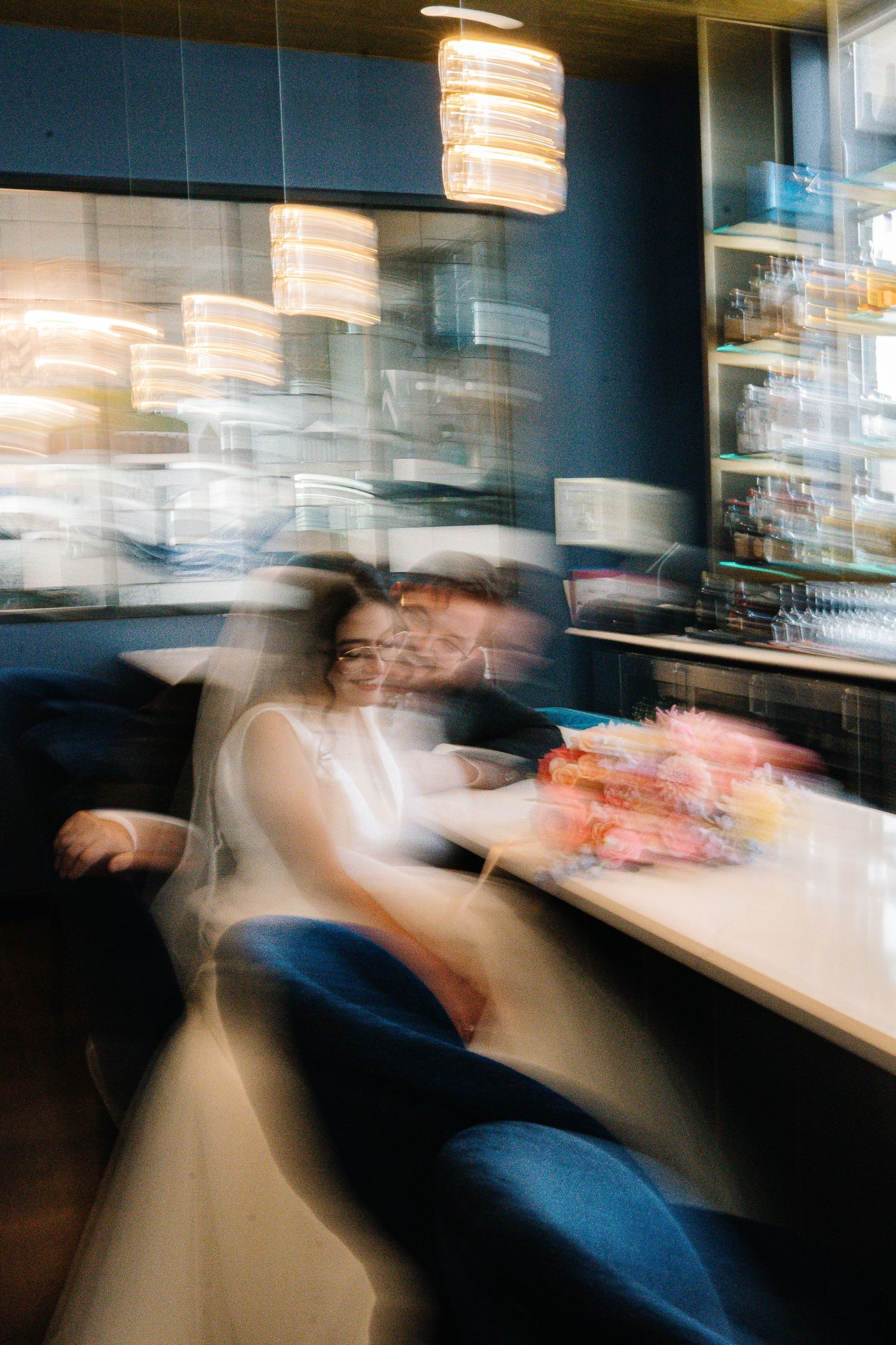 Motion blur photo of guests enjoying a restaurant with hanging pendant lights and modern decor.