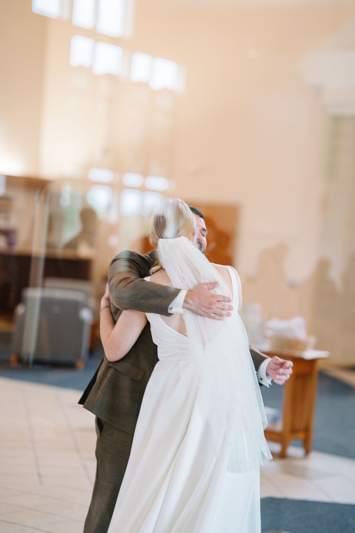 A couple shares a romantic dance moment in a sunlit church hall with warm lighting and wooden floors.