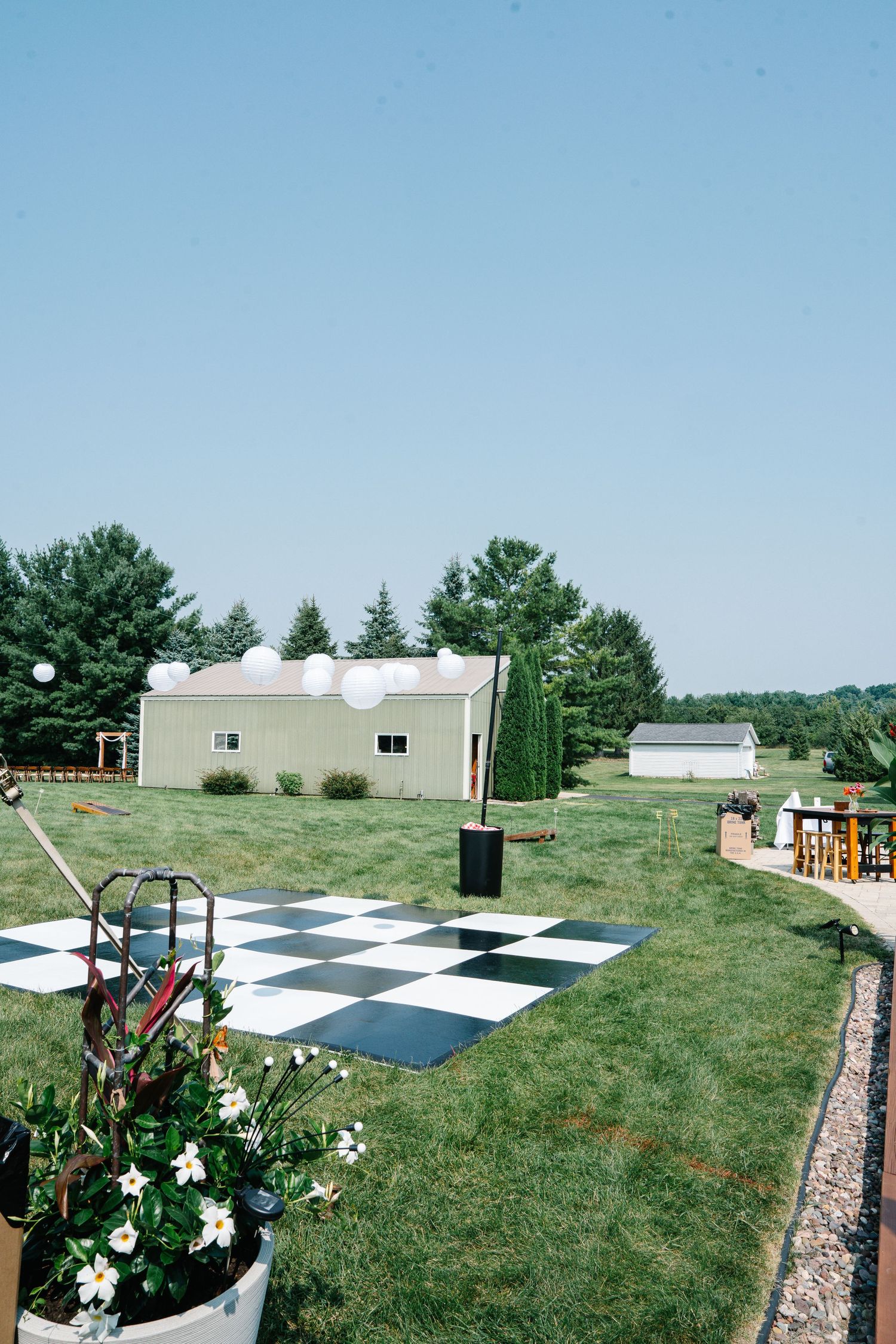 A large outdoor checkerboard pattern set up on grass with white and black squares surrounded by flowers and trees.