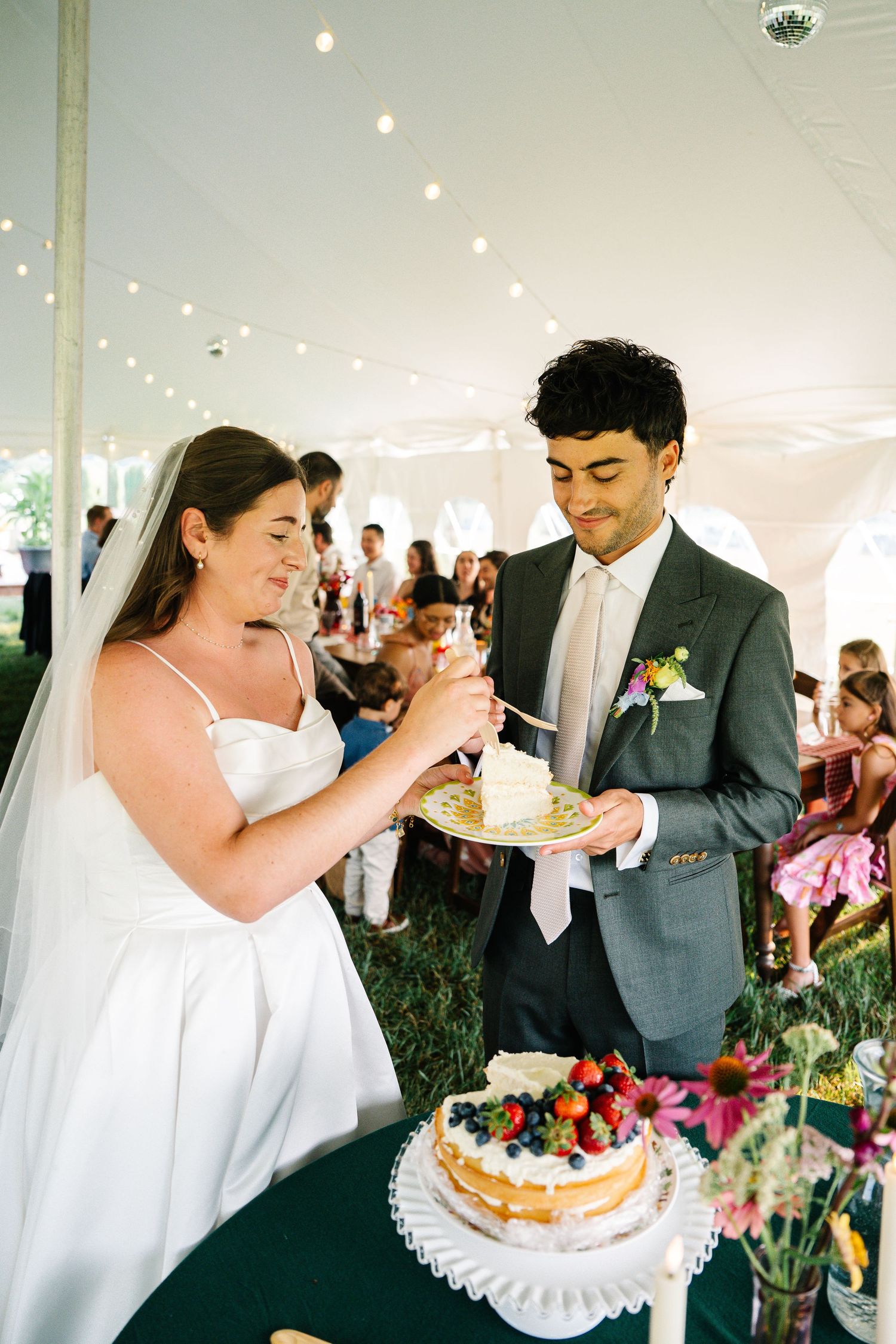 A sequence of wedding reception photos showing a couple sharing cake under a white tent with string lights.