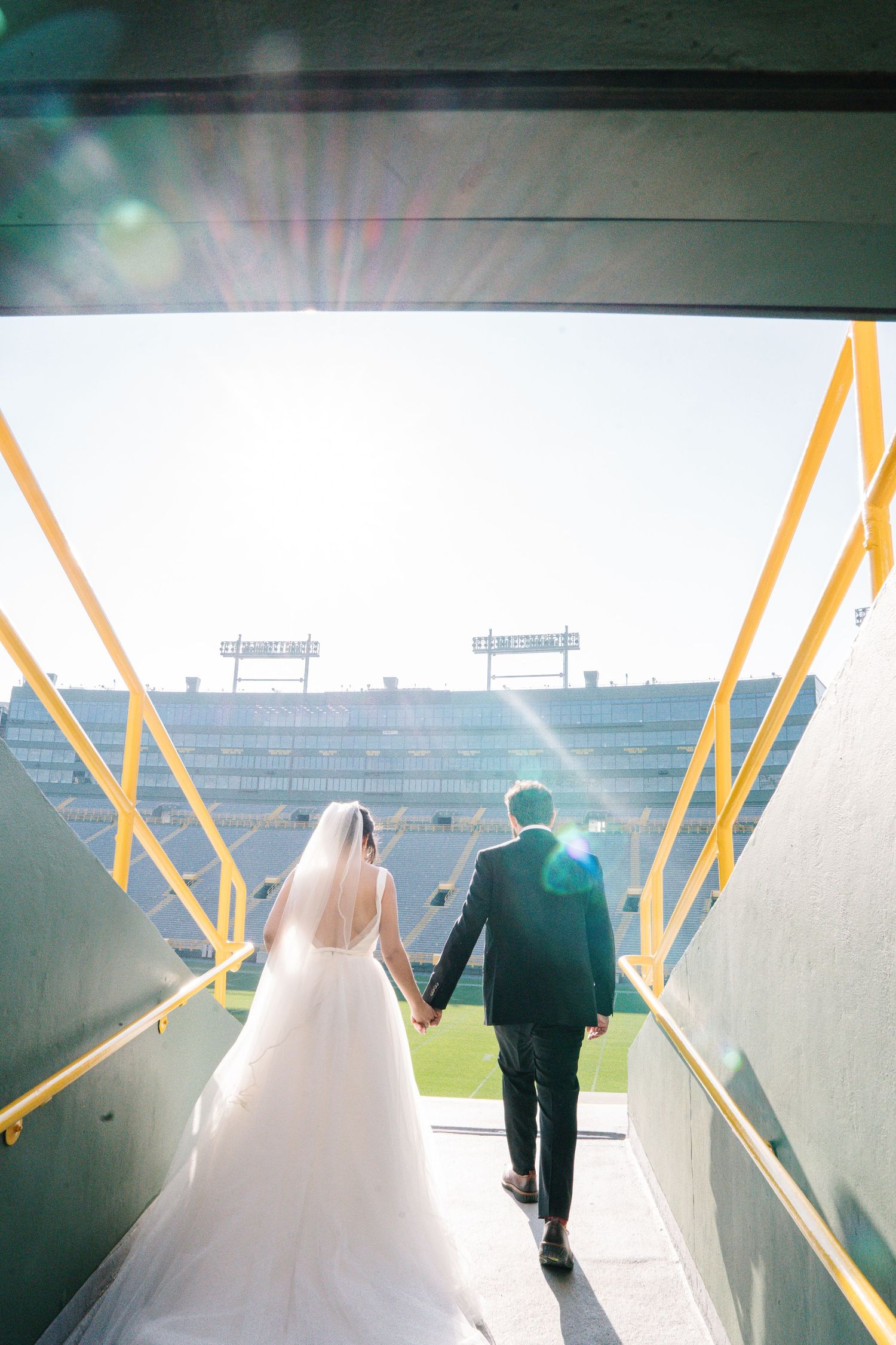 A bride and groom walk through a modern corridor with yellow handrails in an artistic wedding photograph series.