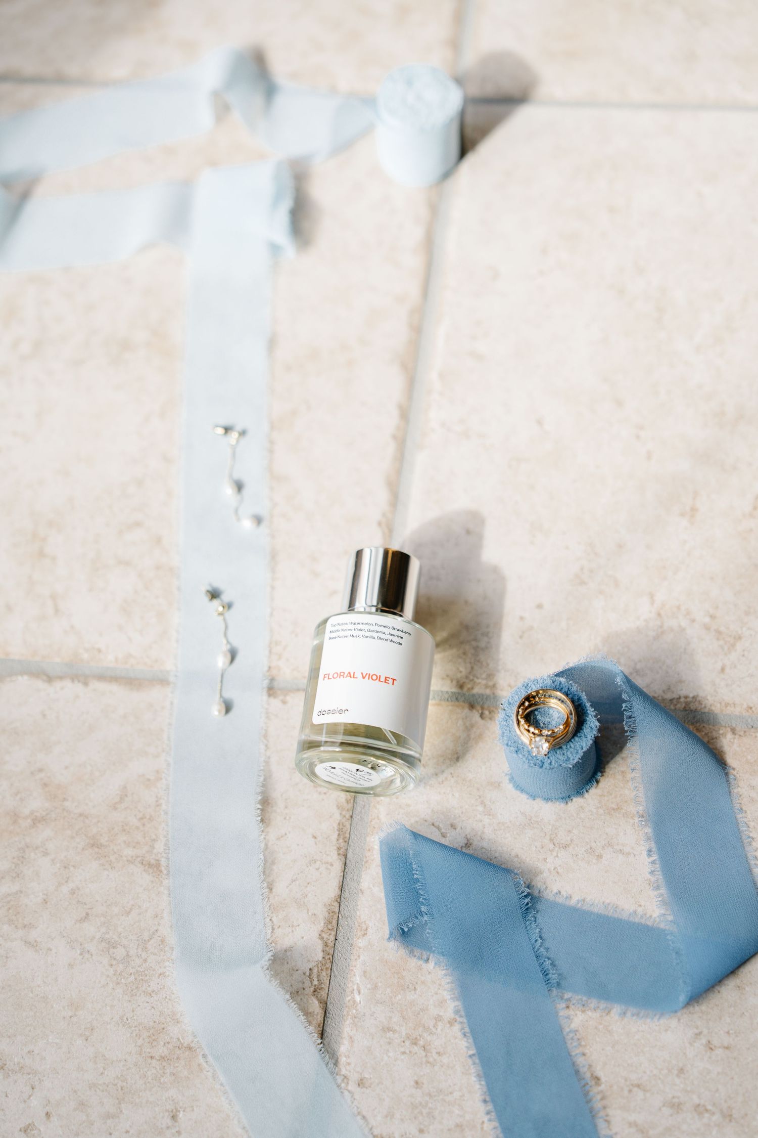 Elegant perfume bottle with light blue silk ribbons arranged on white marble surface.