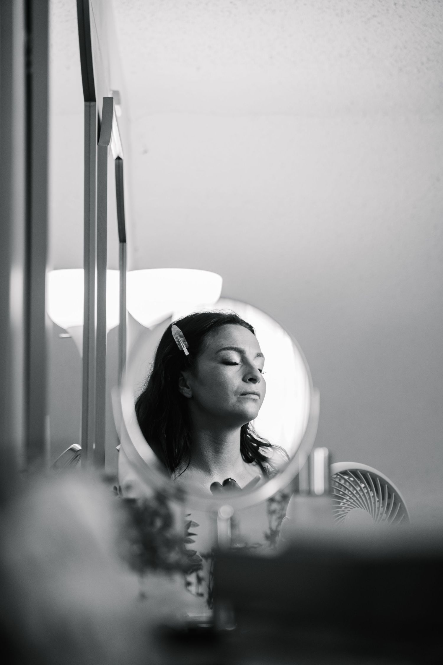 A black and white reflection in a circular mirror shows a serene expression with closed eyes and dark hair.