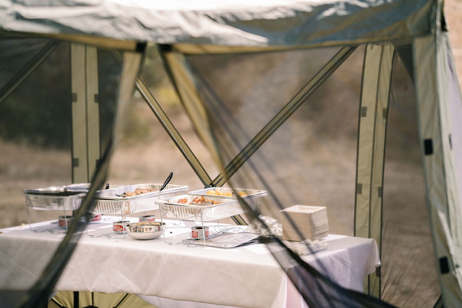 Wedding reception table setting under a tent with place settings and decorative elements.
