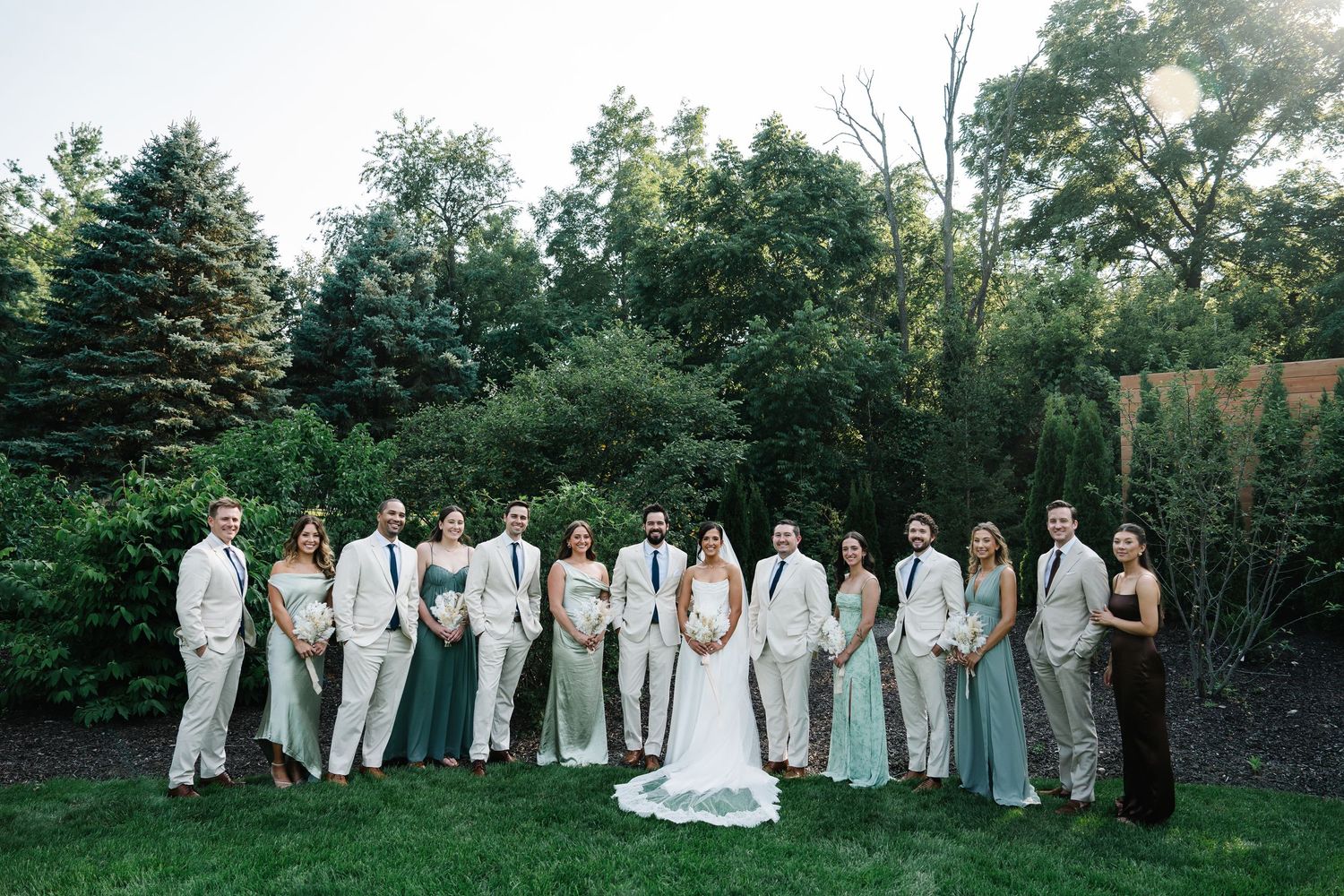 A panoramic wedding party photo sequence showing people in gray and white attire posing in a lush garden setting.