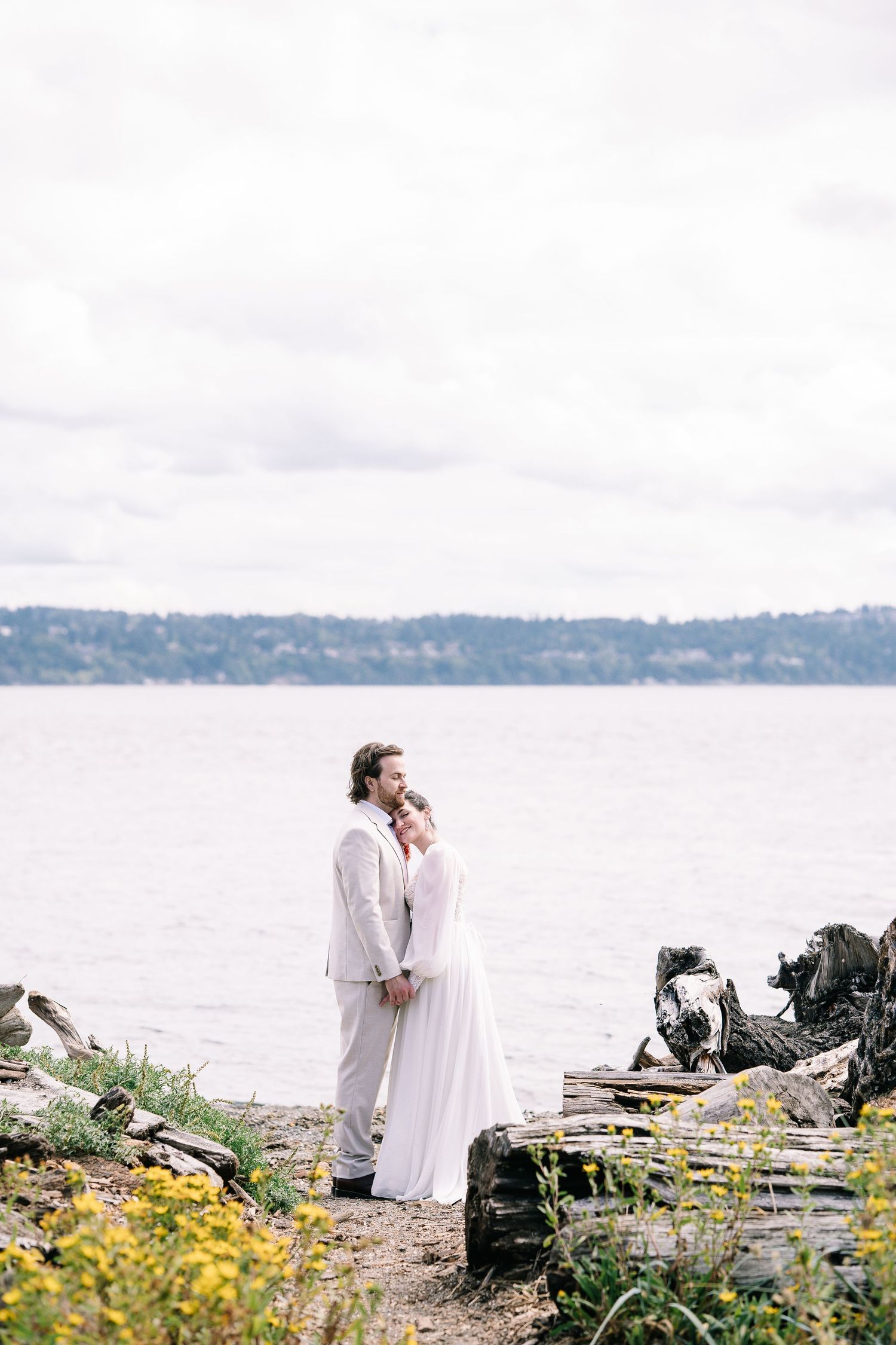 Romantic waterfront scene with couple in white clothing among yellow wildflowers by the ocean.