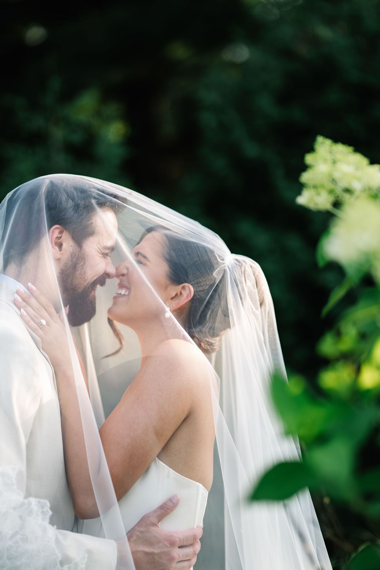 A romantic wedding couple shares an intimate kiss under a flowing white veil in a garden setting.