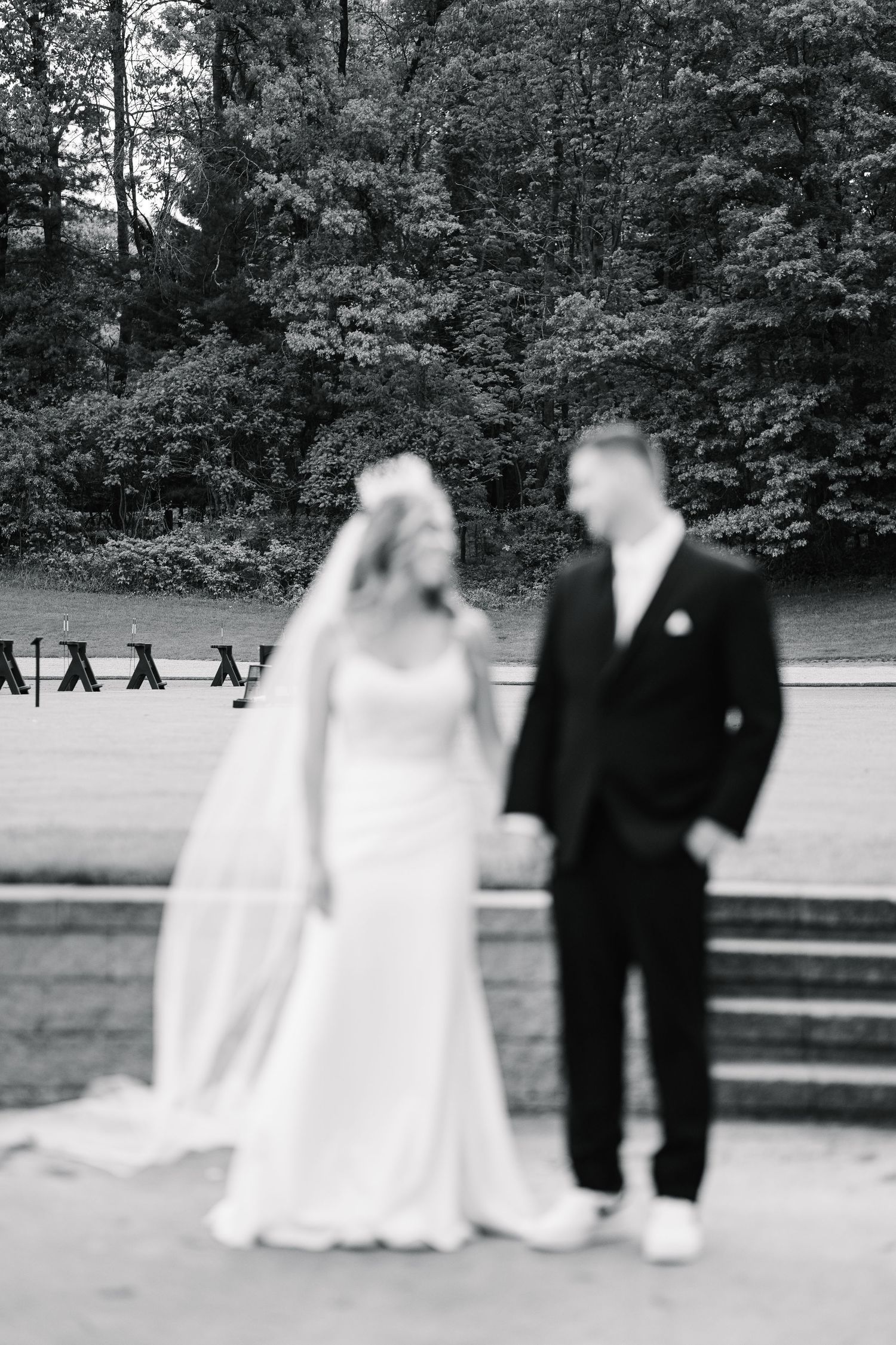 Black and white photo of a wedding couple and guests on a stone patio surrounded by trees.