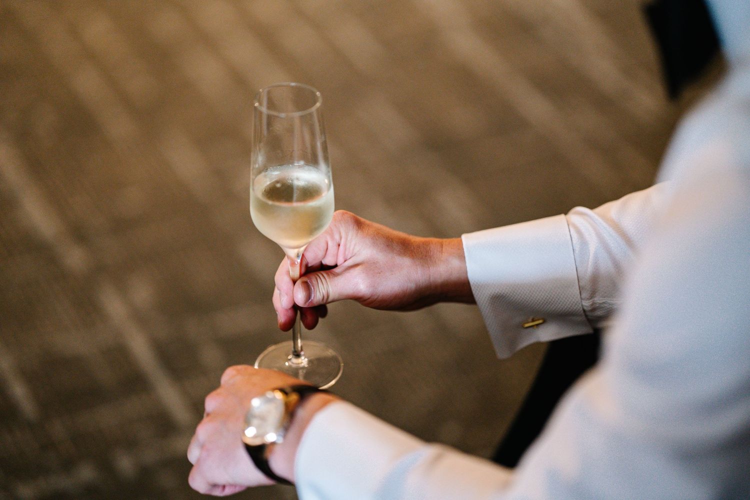 A hand holding a glass of white wine in natural lighting against a blurred background.