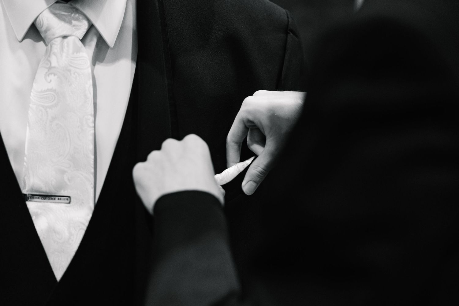 A close-up view of someone's hands adjusting a black bow tie against a white dress shirt.