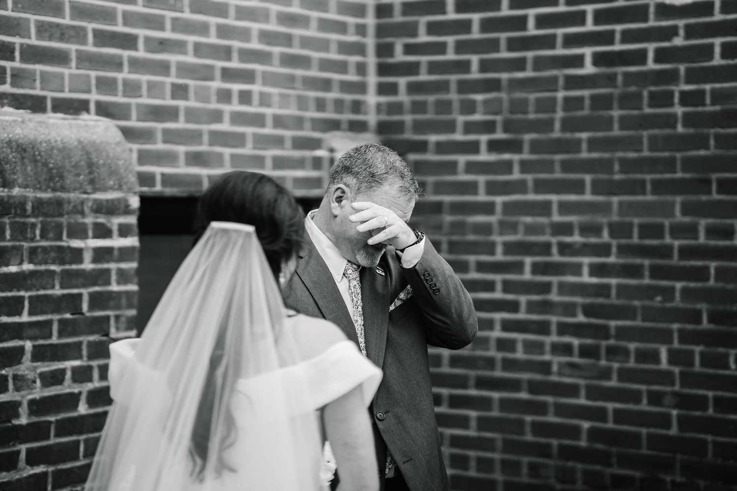 Emotional black and white wedding moment between newlyweds against brick wall during first look.