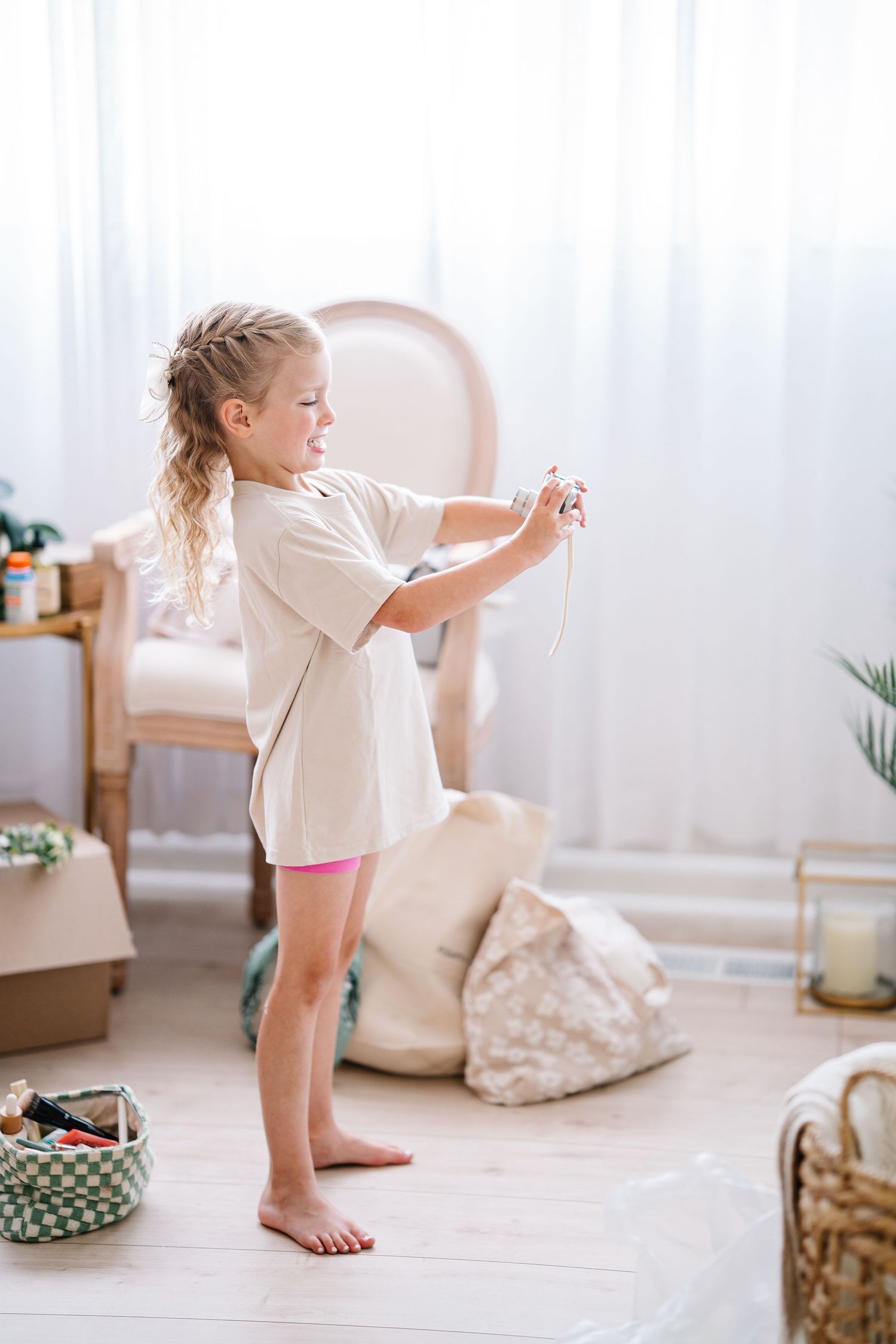 Young child in white shirt playing with string or crafts while standing barefoot in a bright minimalist room.