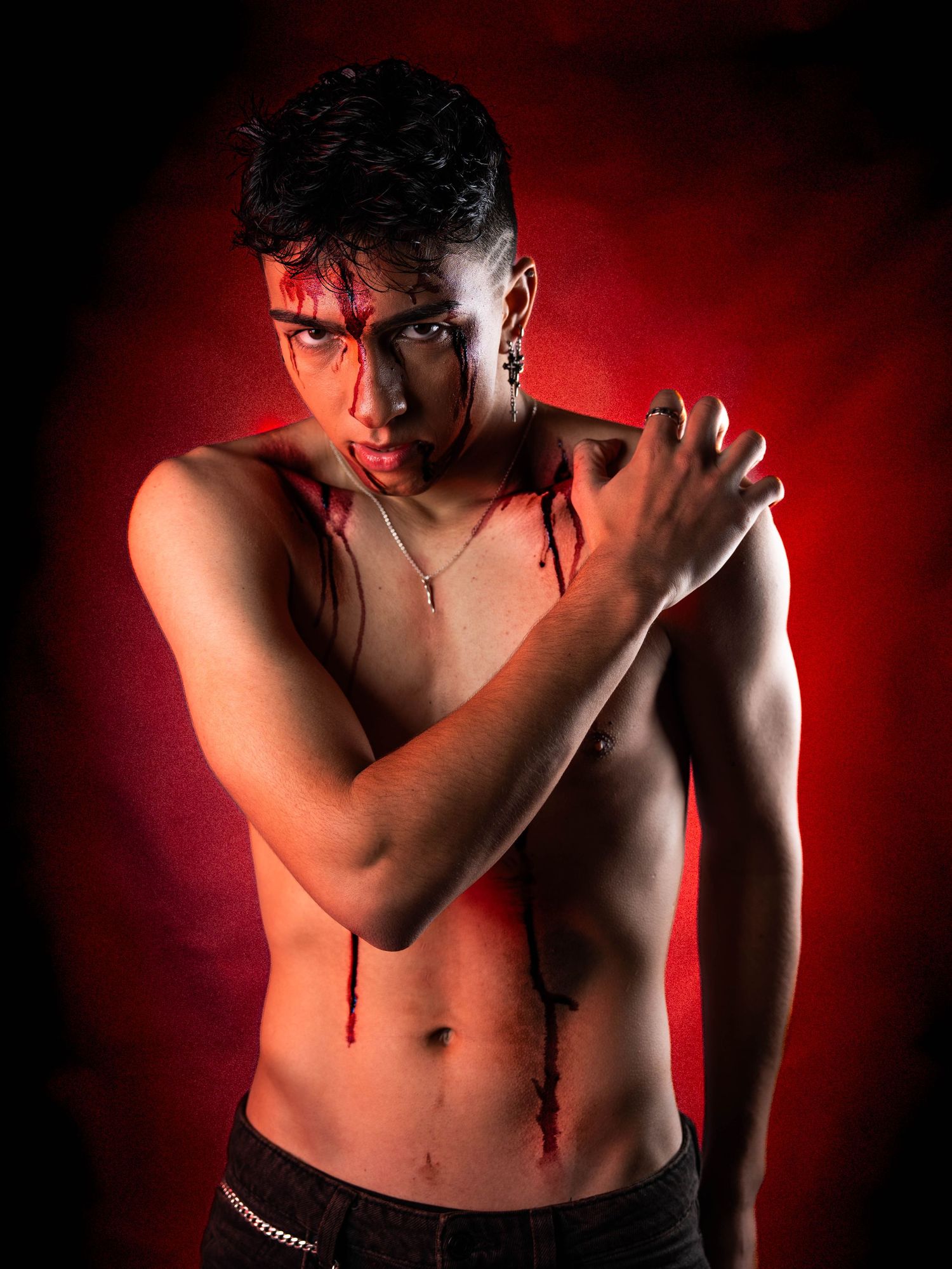 Dramatic portrait of shirtless figure with fake blood effects against red background.