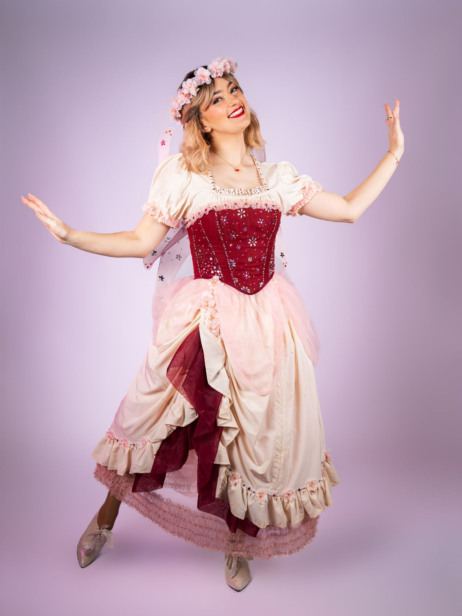Model in vintage-style pink and burgundy dress poses playfully against purple backdrop.