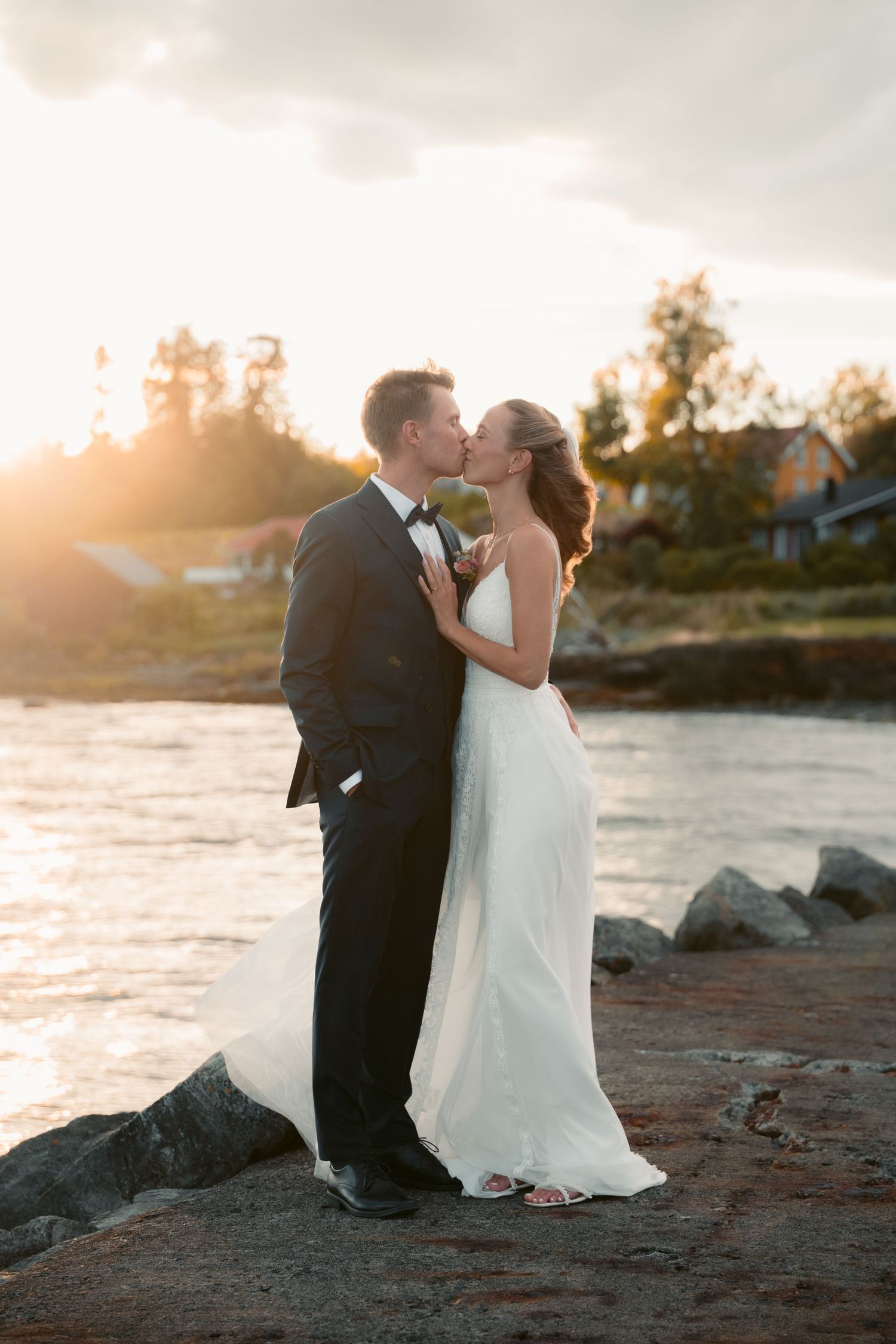 Newlyweds share an intimate moment on a rocky beach at sunset with ocean waves in the background.