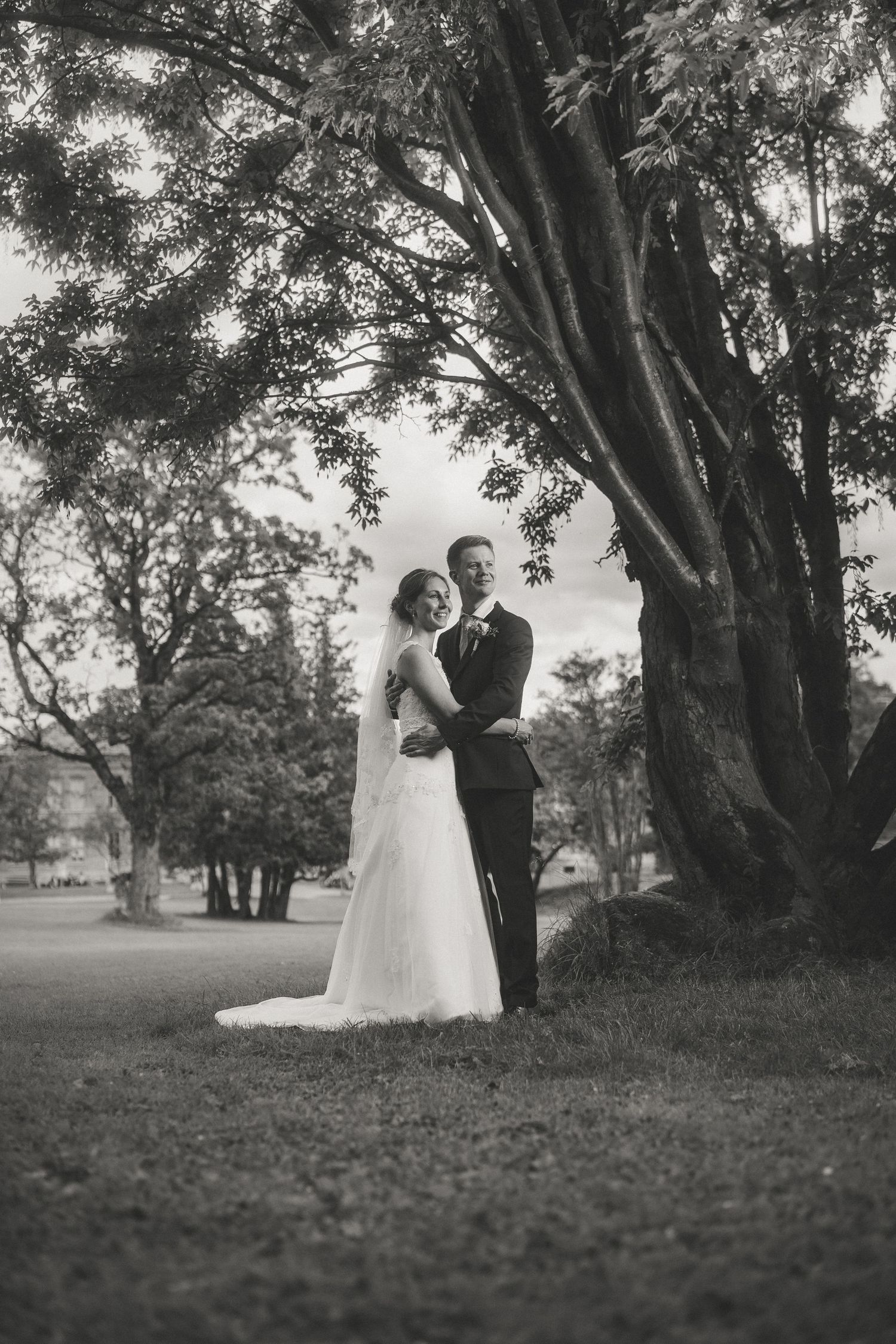Black and white wedding photos of a couple dancing beneath large trees in a park.