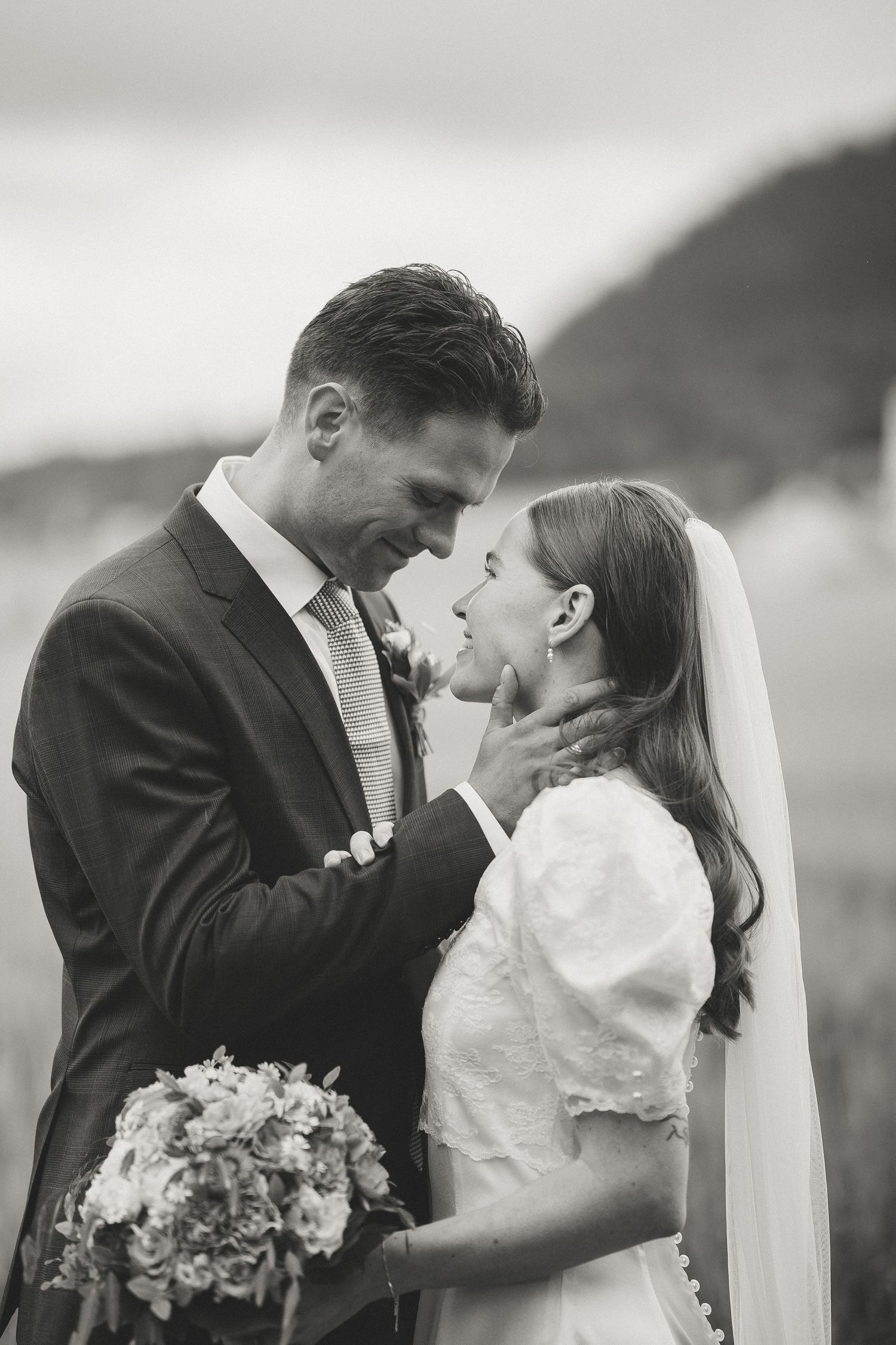 Black and white romantic wedding photo of newlyweds sharing an intimate moment with mountain backdrop.