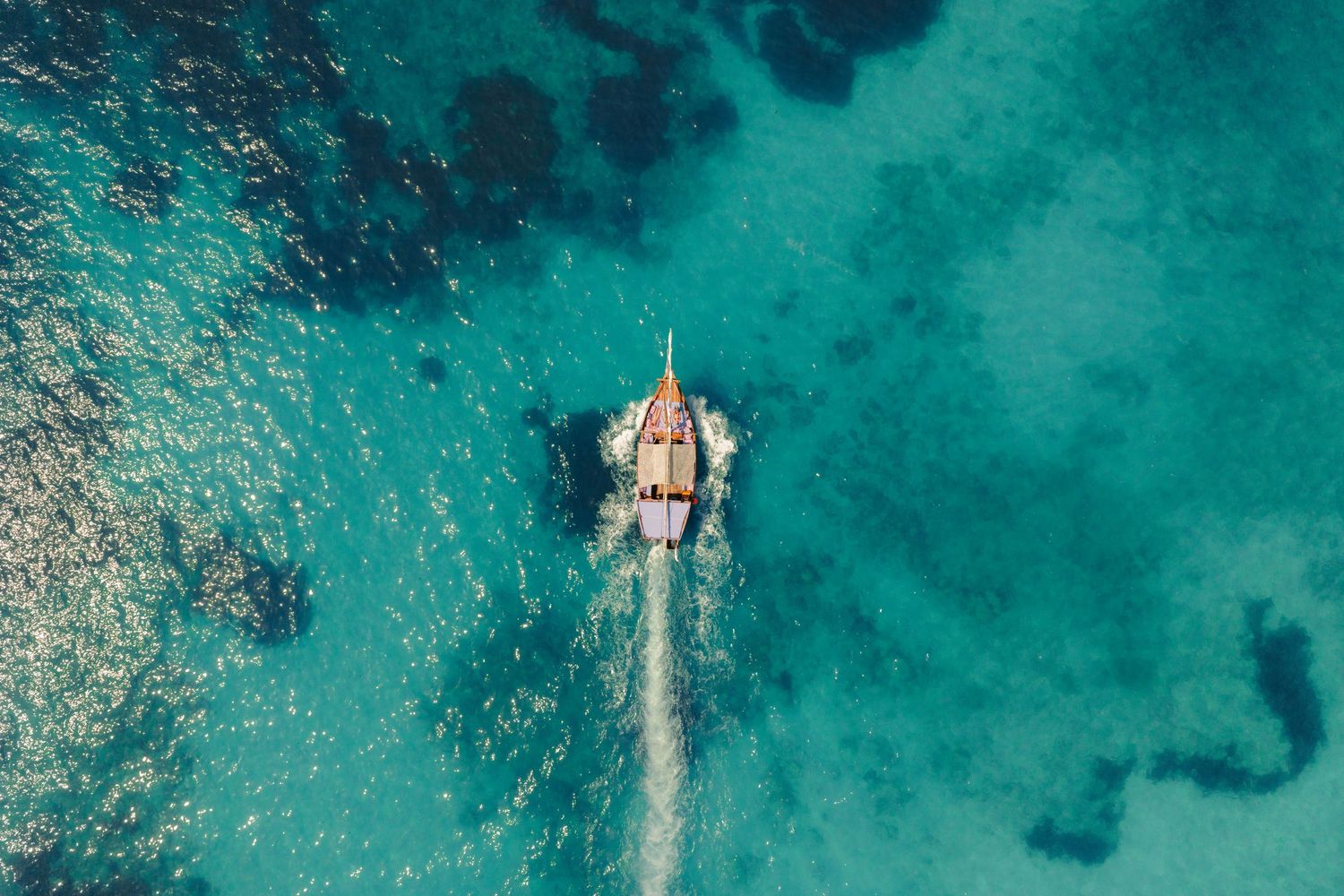 Aerial view of a small boat navigating crystal-clear turquoise waters near a coral reef.