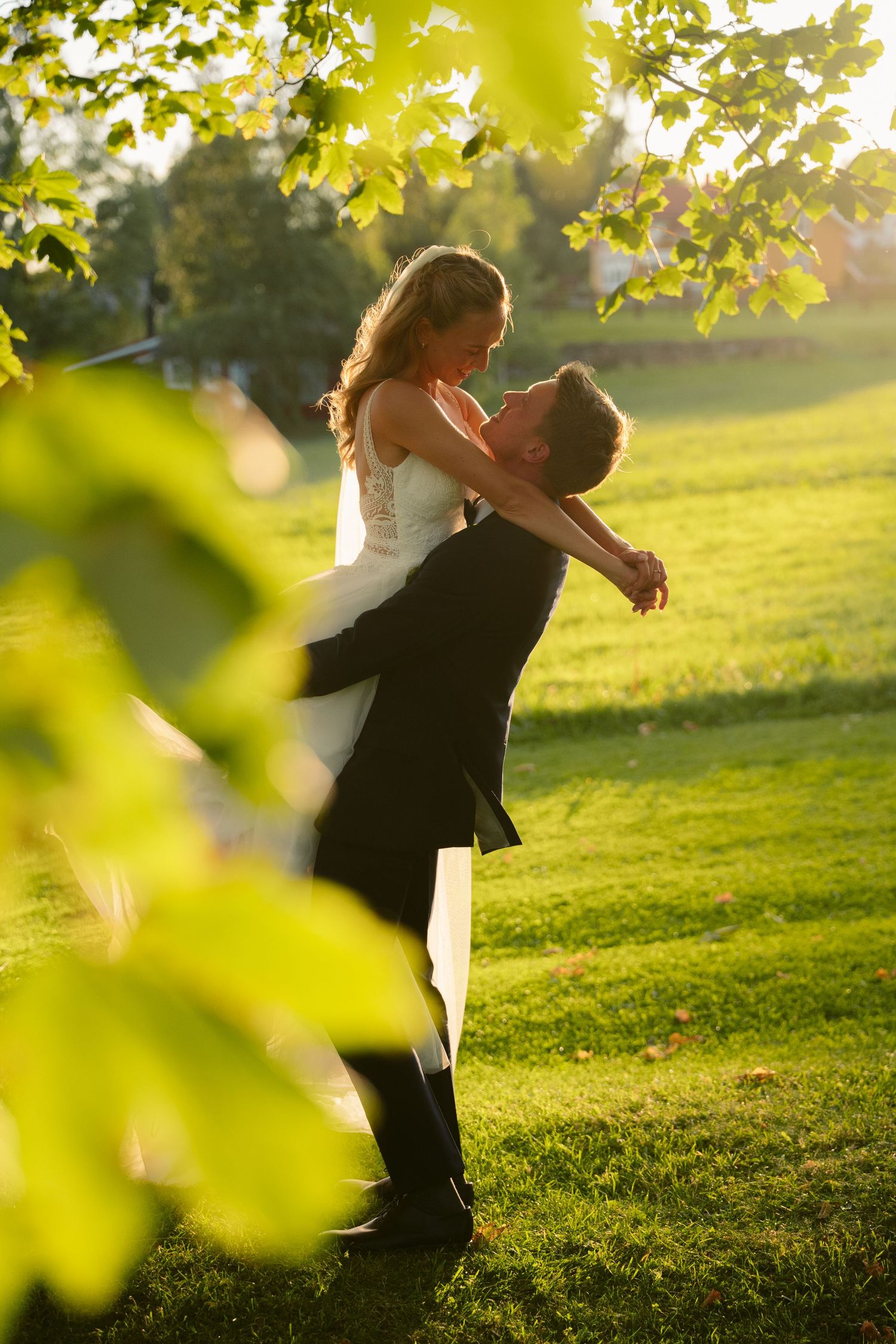 Romantic couple embraces in a sunlit meadow during golden hour with green leaves framing the scene.