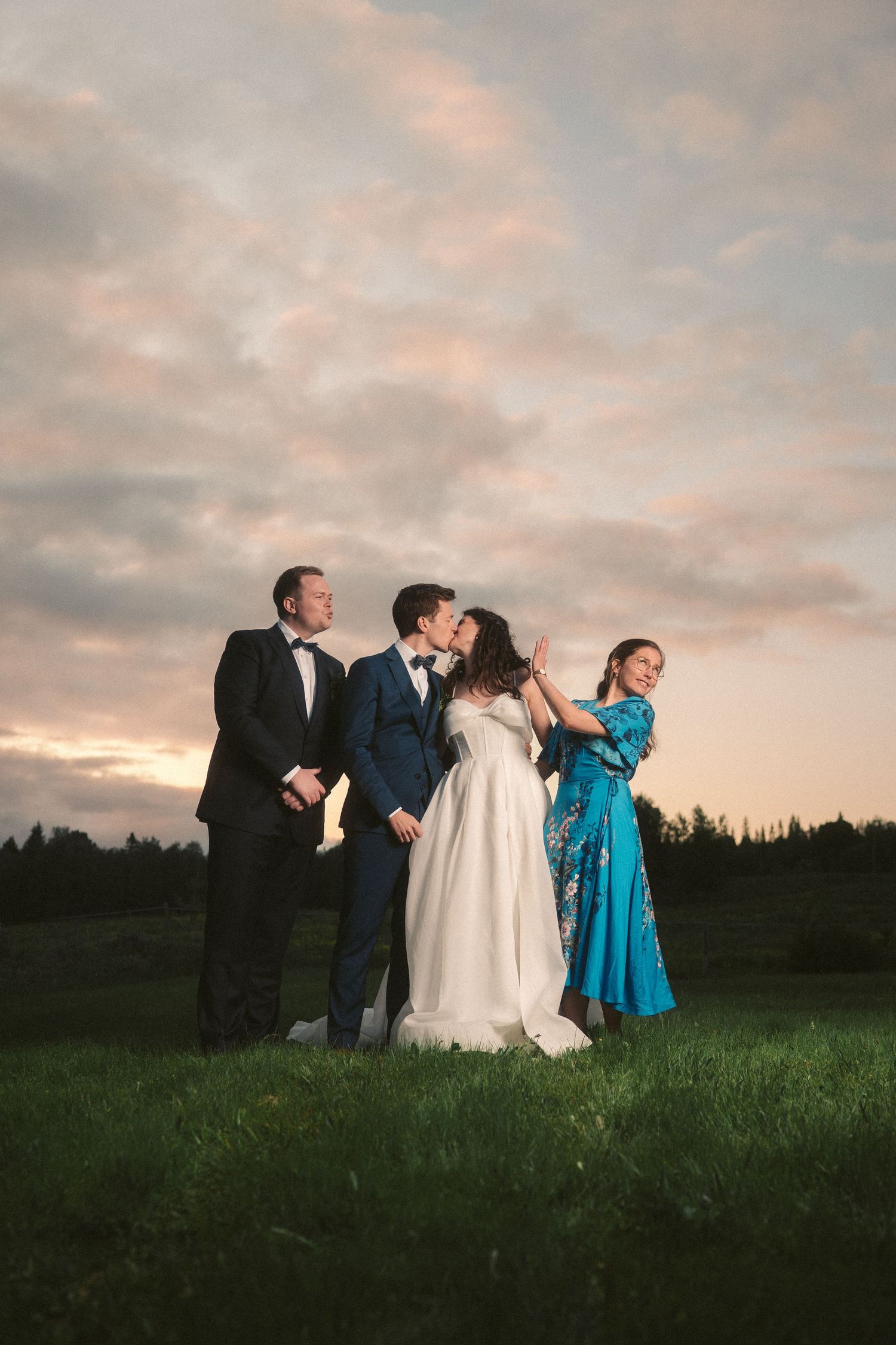 Wedding party celebrates in a field during sunset with dramatic sky backdrop.