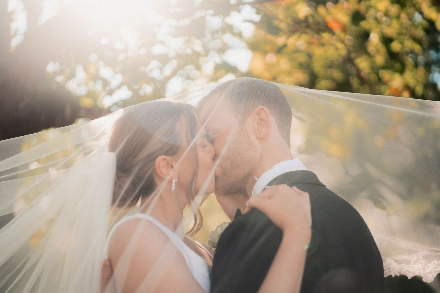 Intimate wedding moment captured with sunlight and flowing veil.