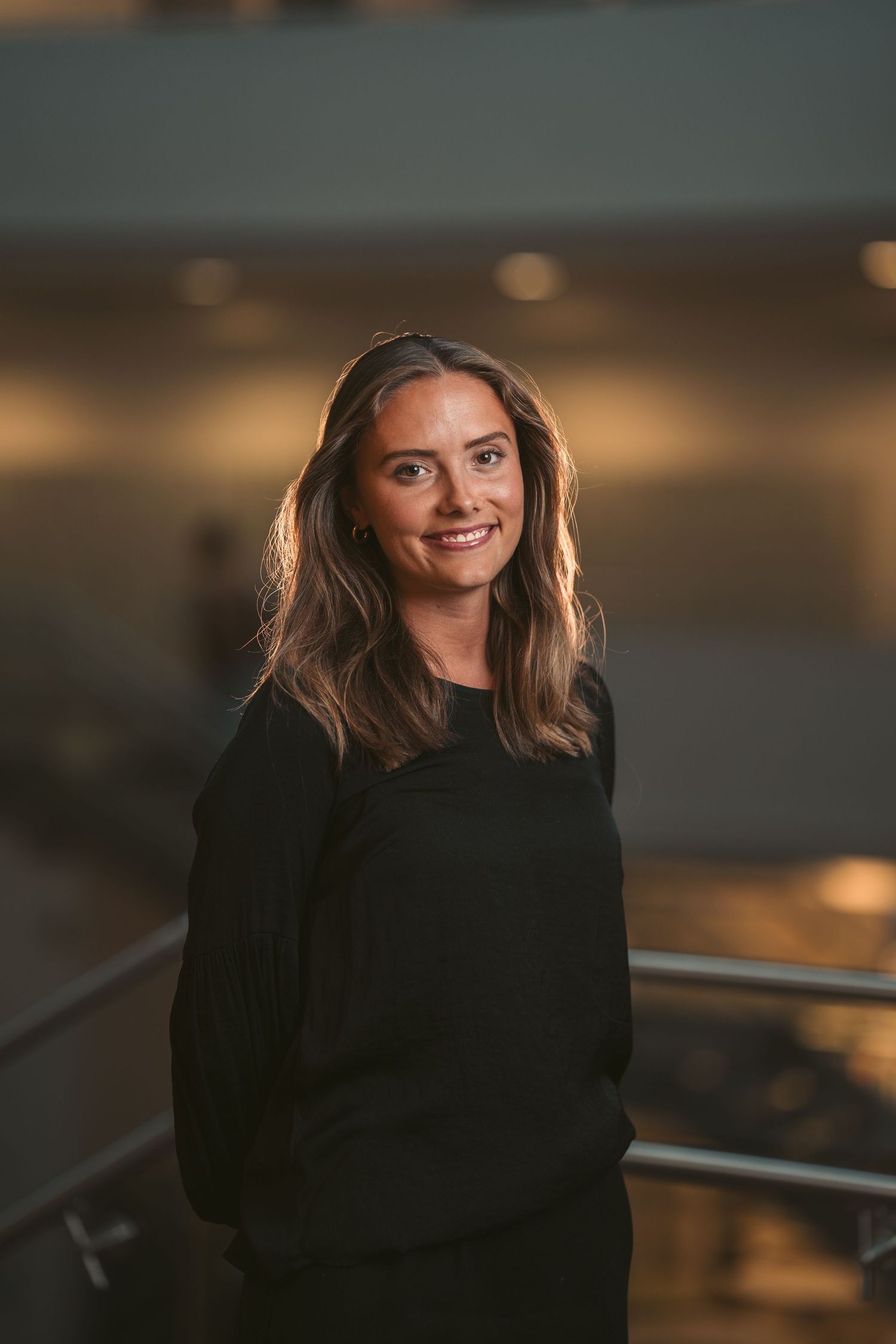 A portrait of someone in a black outfit smiling against a warm atmospheric background.