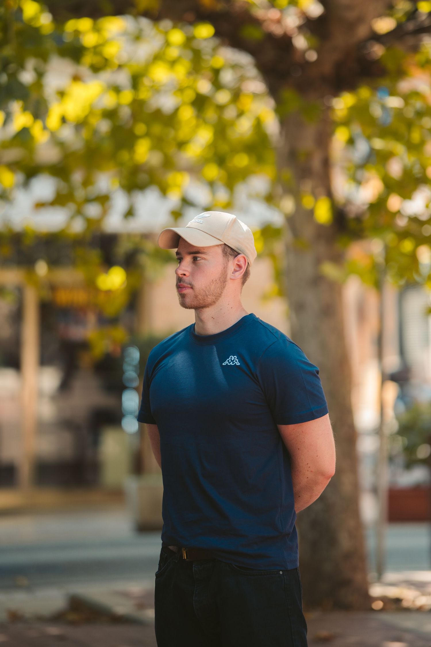 Person in blue t-shirt and baseball cap standing in front of yellow autumn foliage.