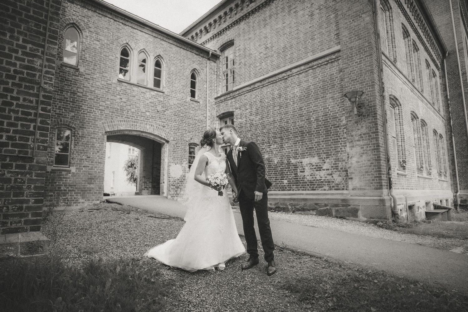 Wedding couple poses against brick walls in dramatic black and white photography.