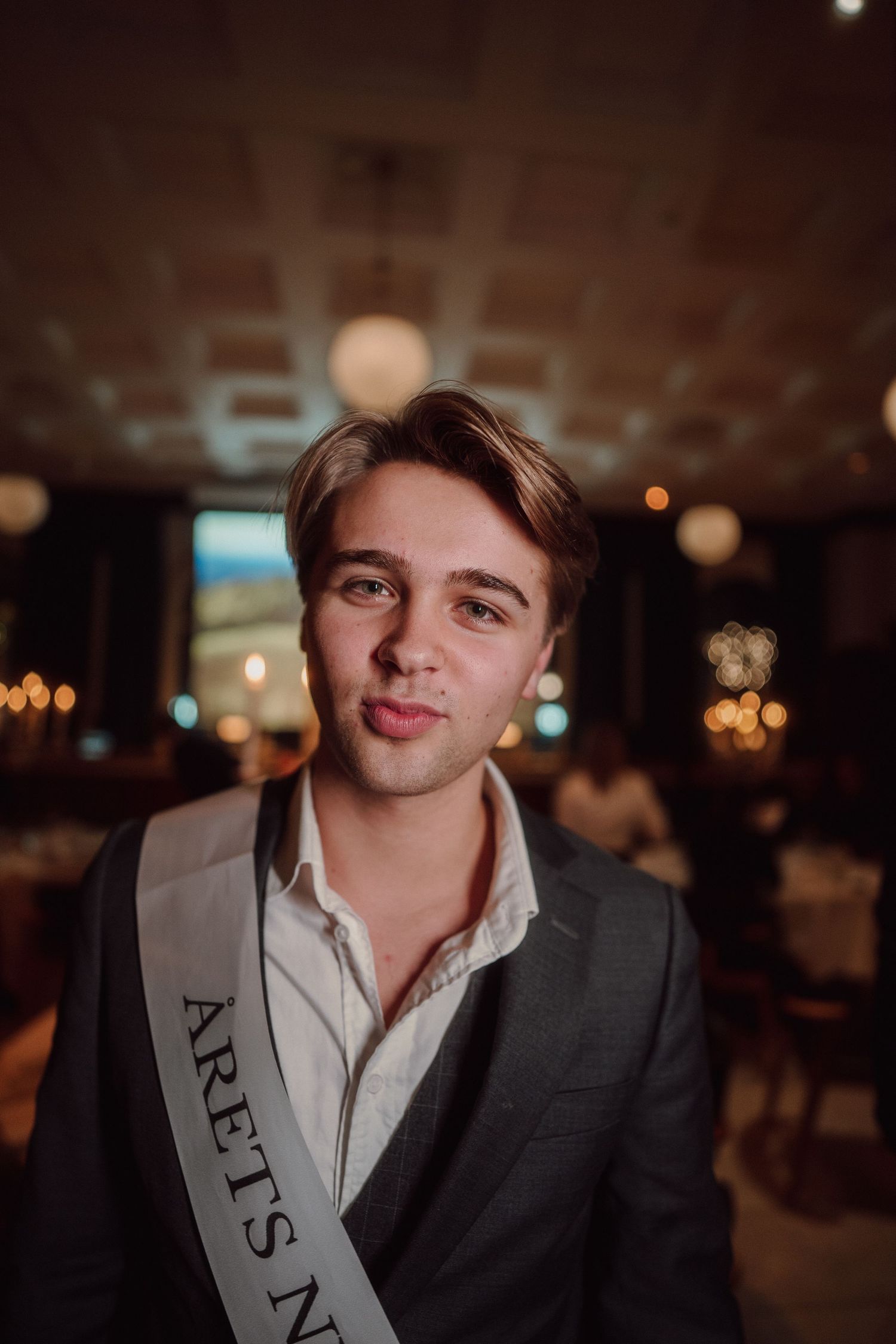 Young person wearing formal attire and sash at evening celebration event.