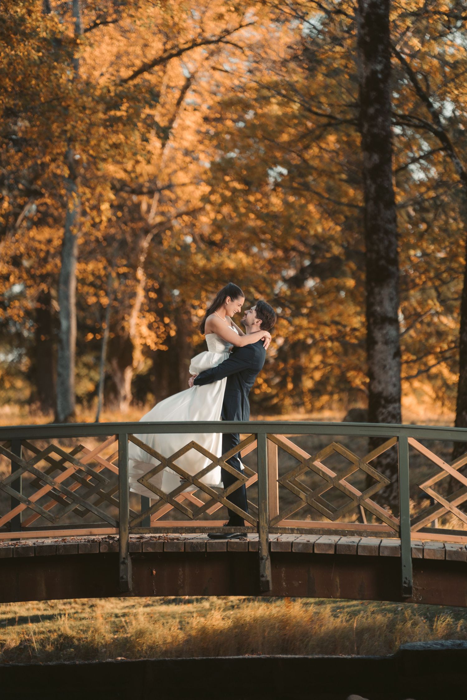 Couple shares intimate moment on rustic bridge amid fall colors at sunset.