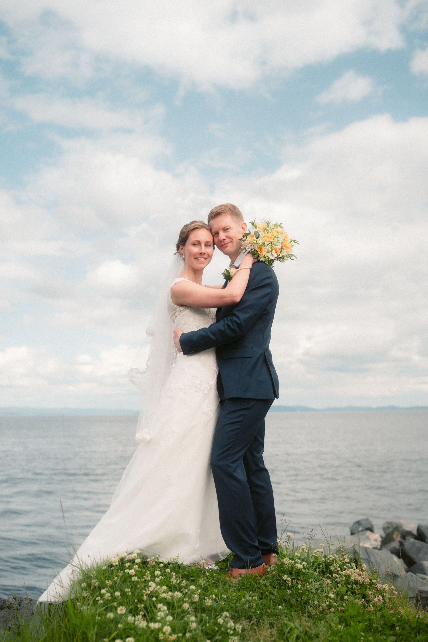 A romantic wedding photo series showing a couple embracing on a grassy hill overlooking the ocean.