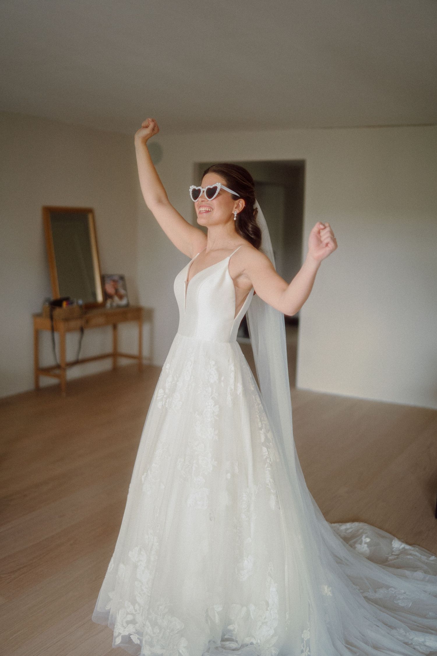 A bride in a flowing white wedding gown dances joyfully in a bright indoor space.
