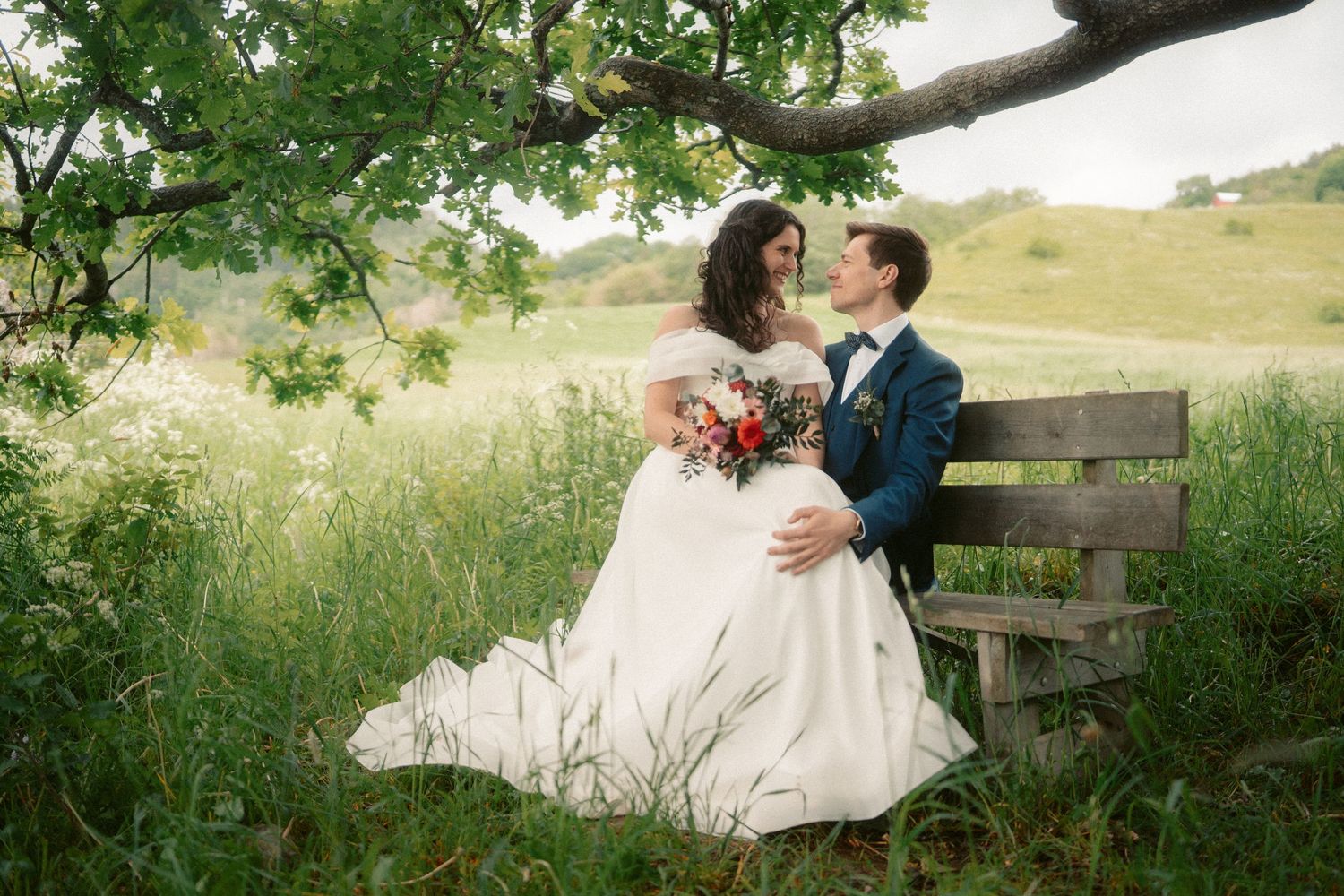 Romantic wedding photos of a couple sitting and embracing on a wooden bench outdoors.