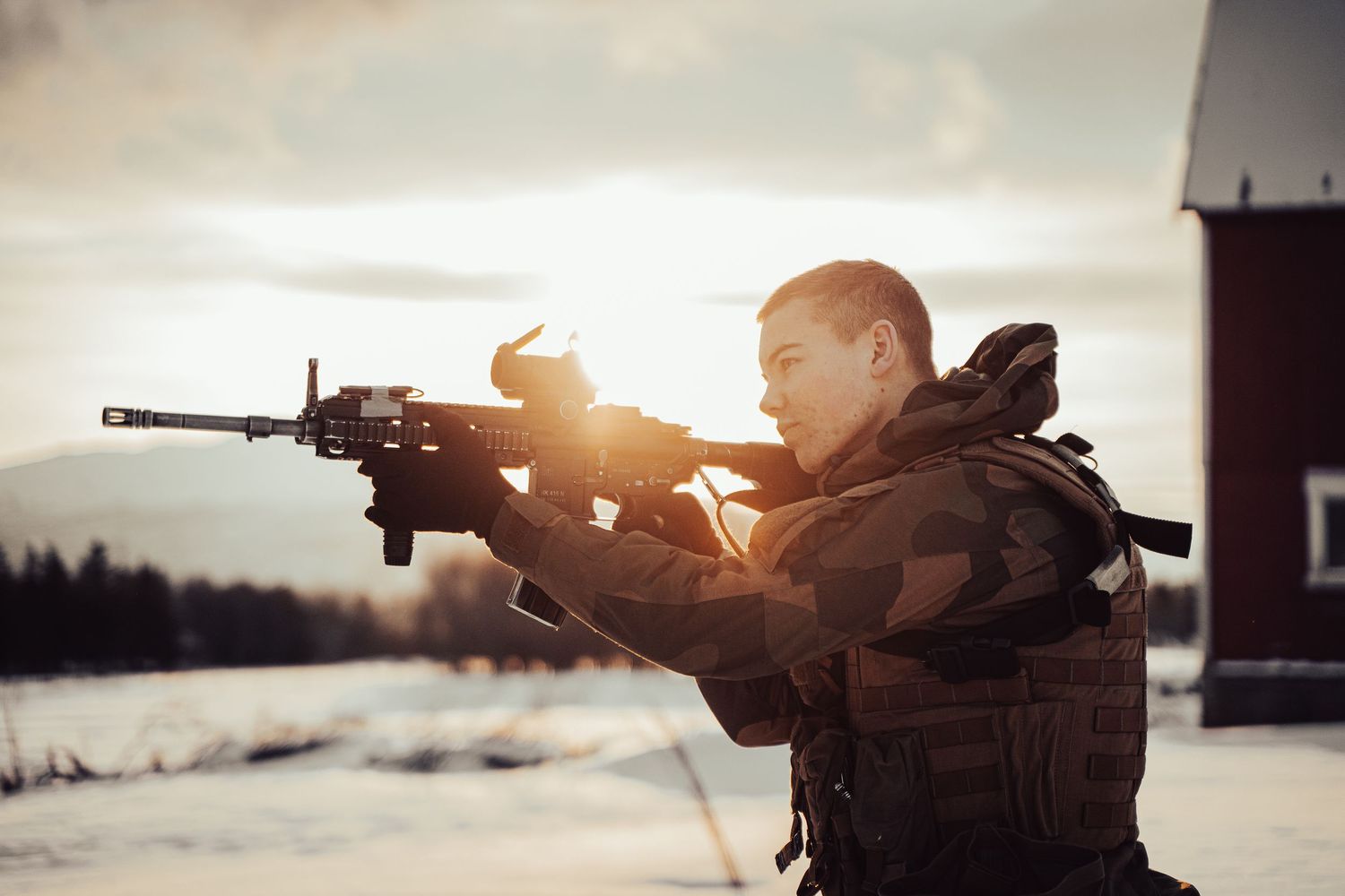 Silhouetted soldier with rifle training at sunset in snowy conditions.